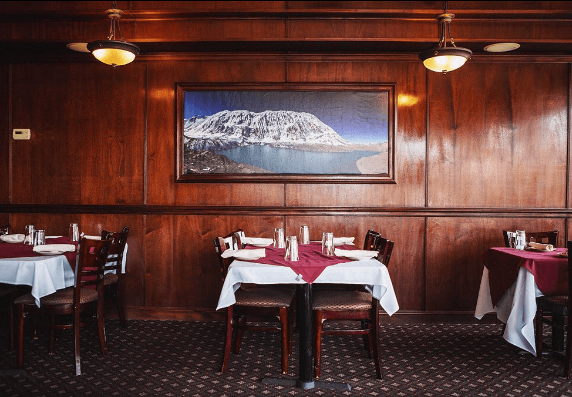 A crow perched on a pipe against an orange sky.