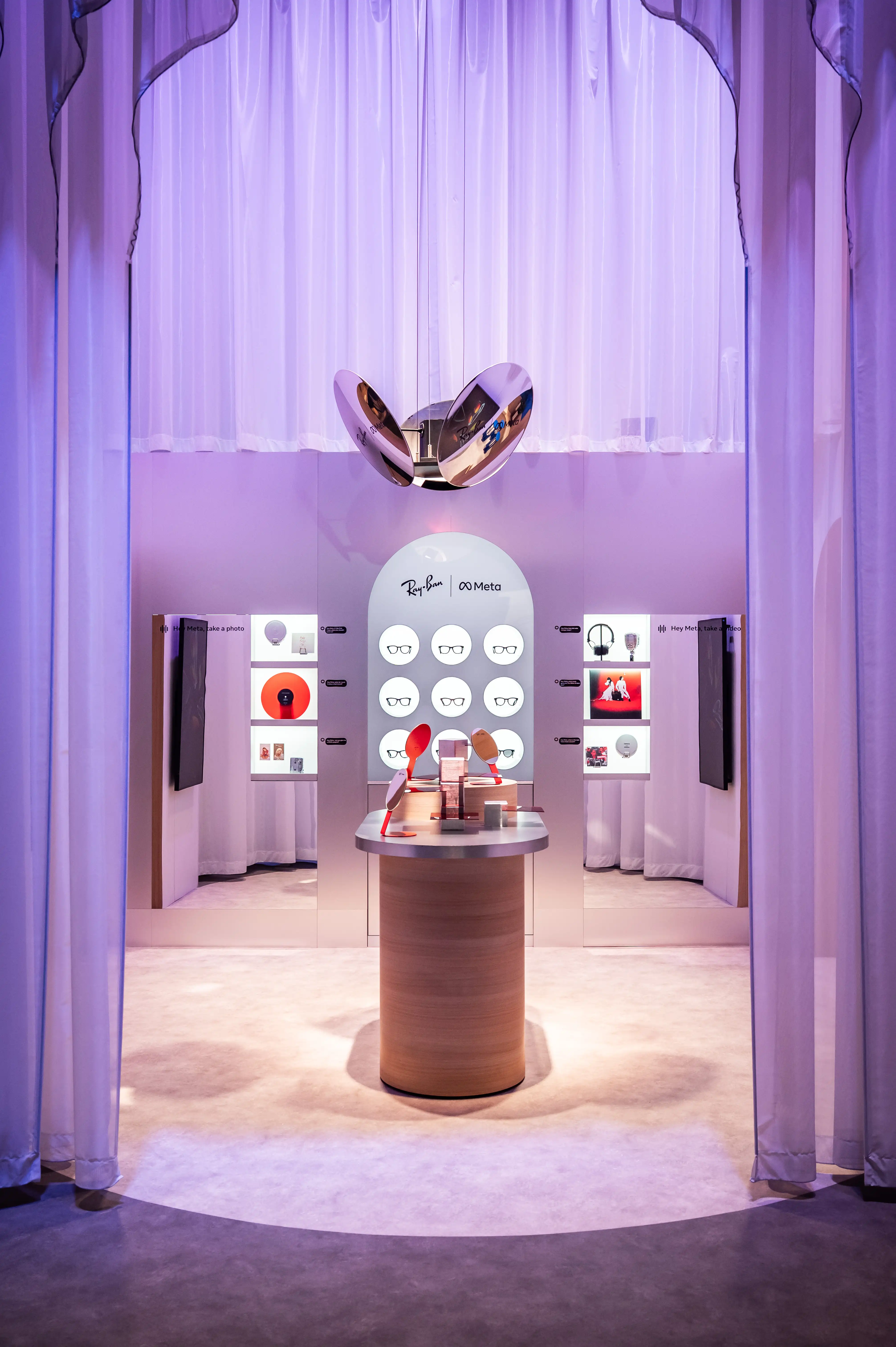 Ray-Ban Meta display with glasses on a white arched panel and chrome sculpture above a round wooden counter.
