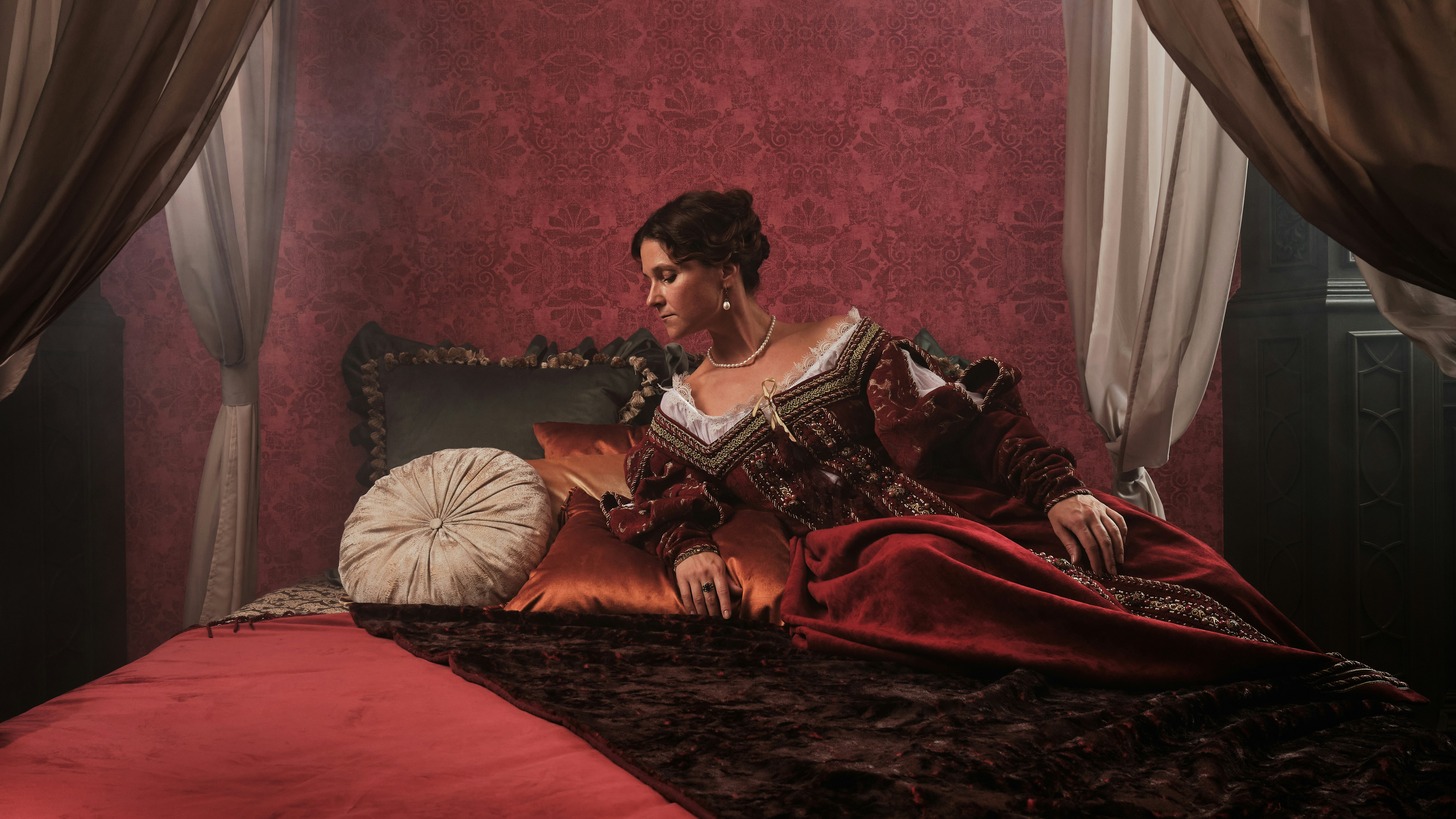 A royal-style bed with a woman resting on it, in a luxurious bedroom setting.