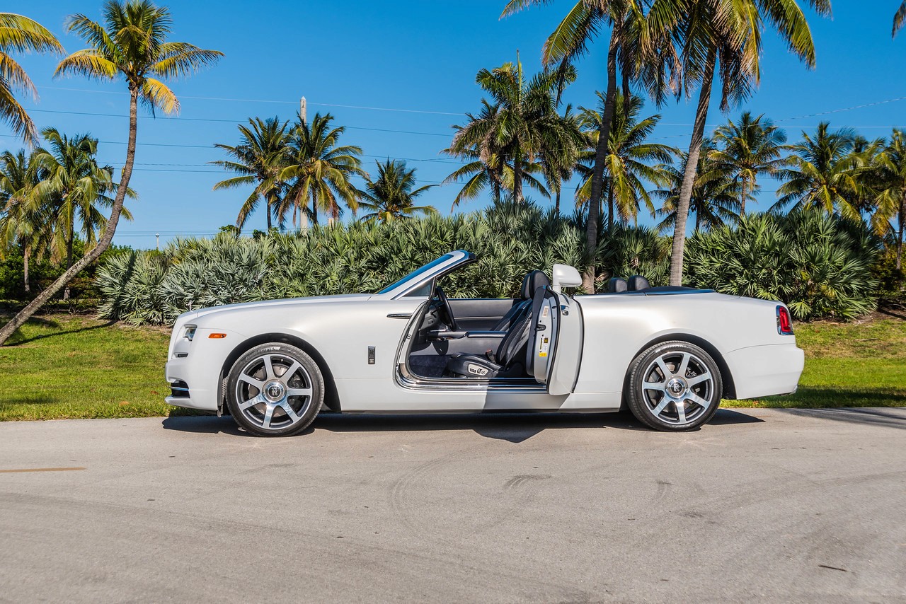 Rear-side perspective of the Rolls-Royce Dawn parked in a tropical location, emphasizing its sleek design and luxury presence.