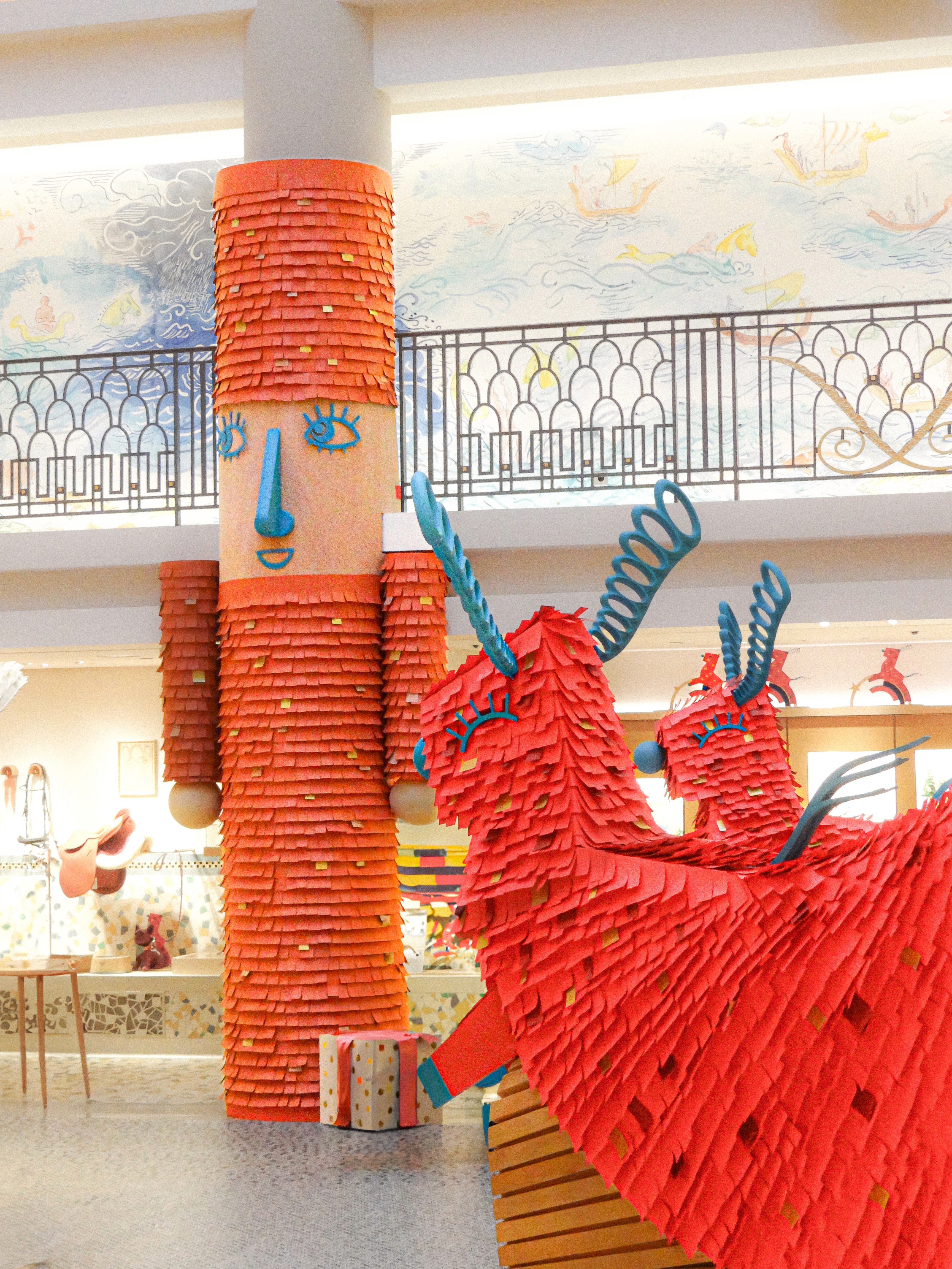 In-store holiday installation for Hermès featuring a tall, orange fringed character and playful reindeer-inspired wooden toys, designed by WM Paris to evoke a sense of childhood wonder within the boutique.