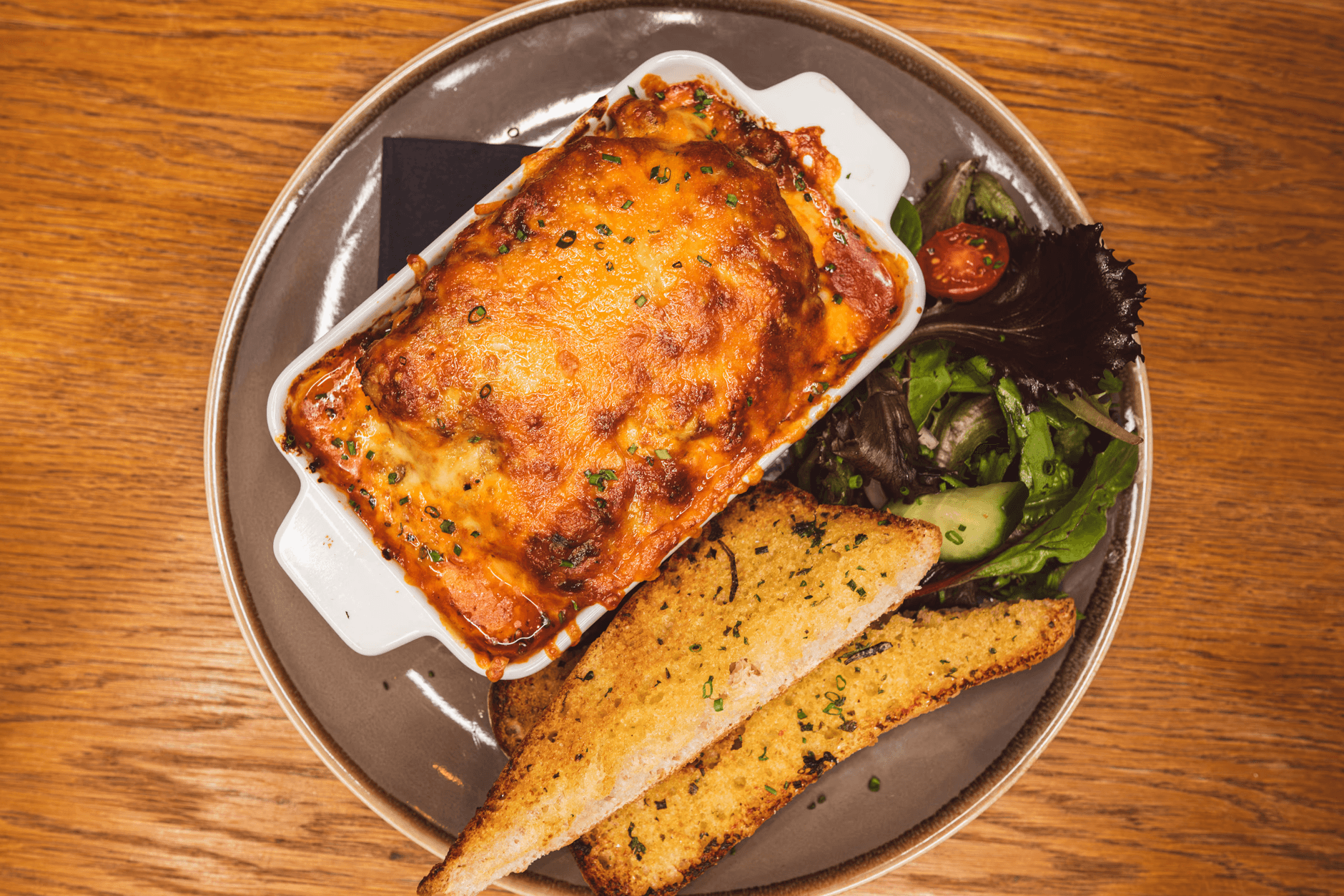 Italian ragu layered pasta sheets in a creamy béchamel sauce topped with grilled cheese, served with garlic bread & salad garnish