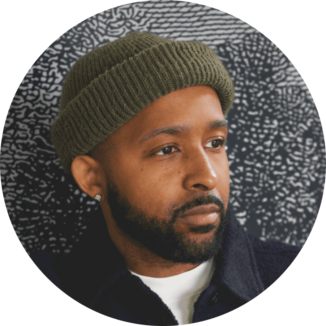 Person wearing a blue puffer jacket and red backpack standing in front of a light blue building on a city street.