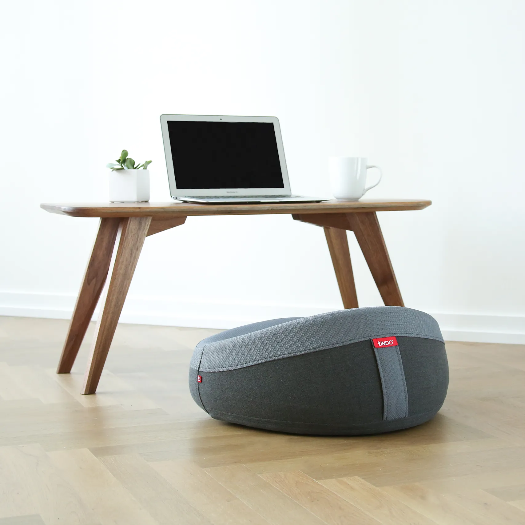 Dark gray UNDO meditation cushion beside a low table with a laptop and cup