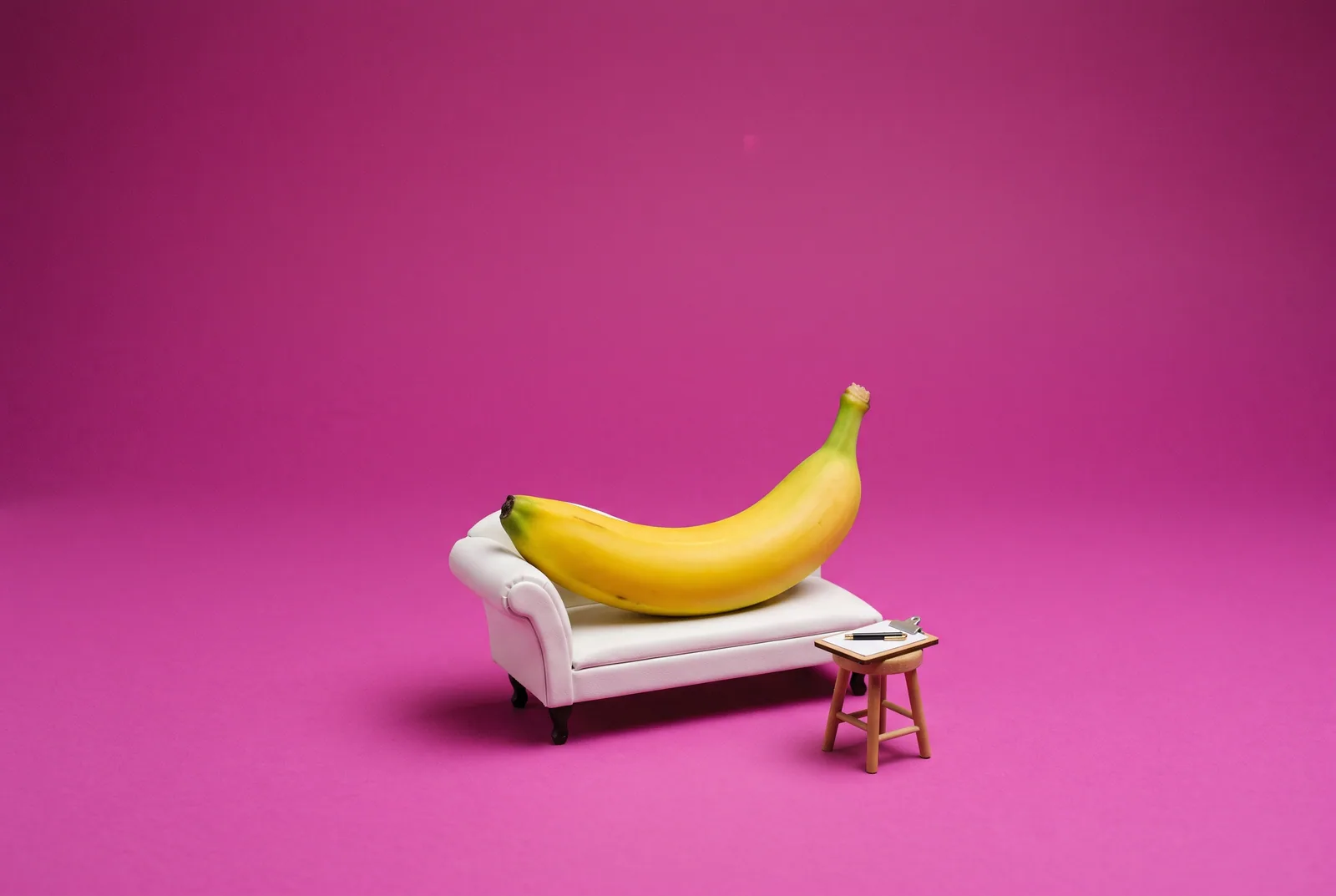 A banana lying on a tiny therapist's couch beside a blank clipboard, asking whether gooning addiction is a real diagnosis