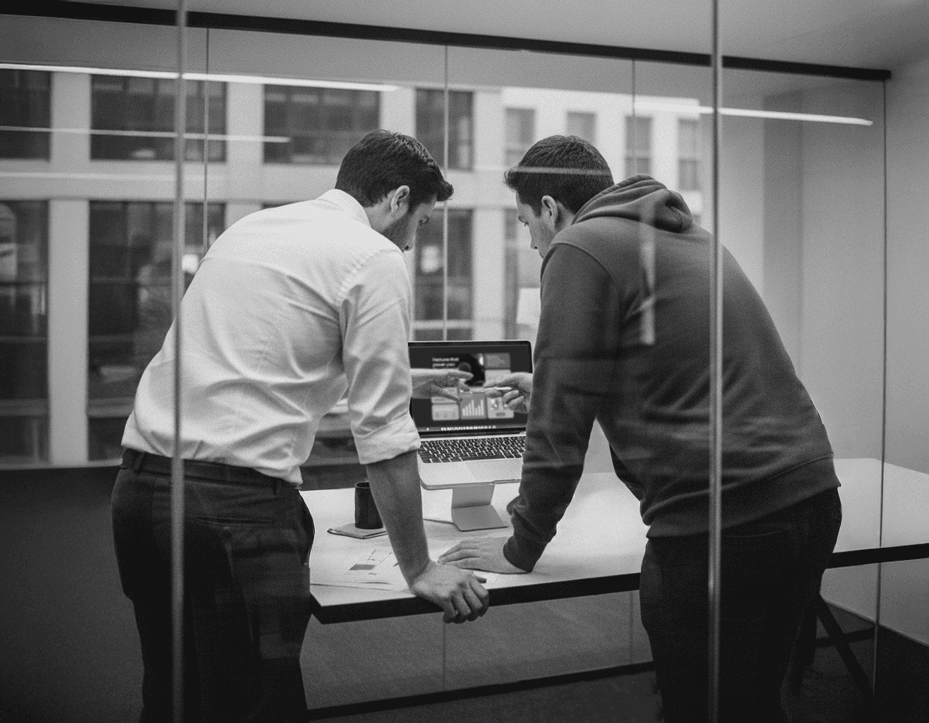 Black and white image of people working at a table with laptops, showing hands gesturing during discussion of digital content displayed on screens, with fabrica® logo in the corner.