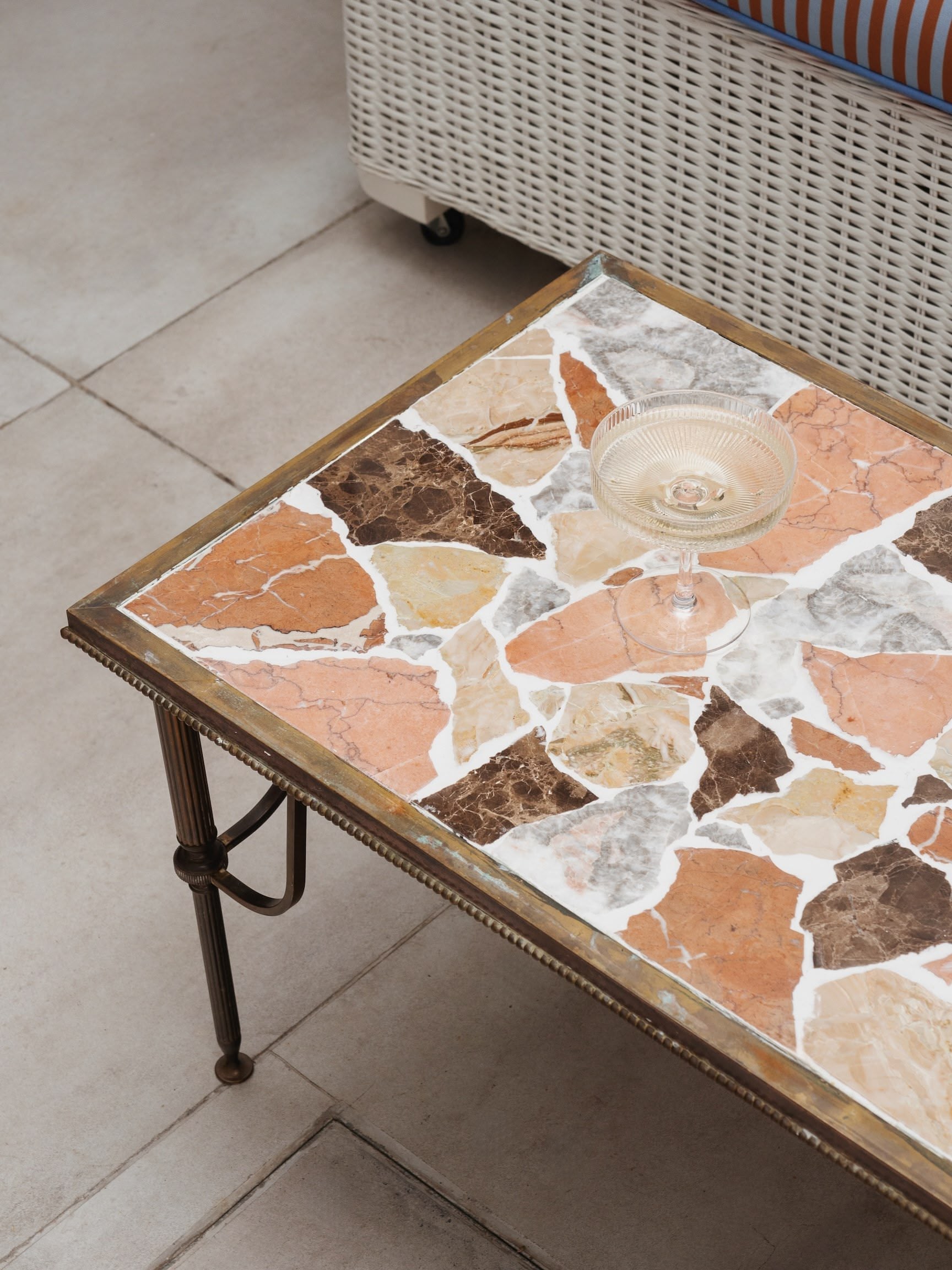 Close-up of a vintage-style table with a mosaic top composed of irregular stone pieces in shades of brown, beige, and pink, with a glass holder on top.