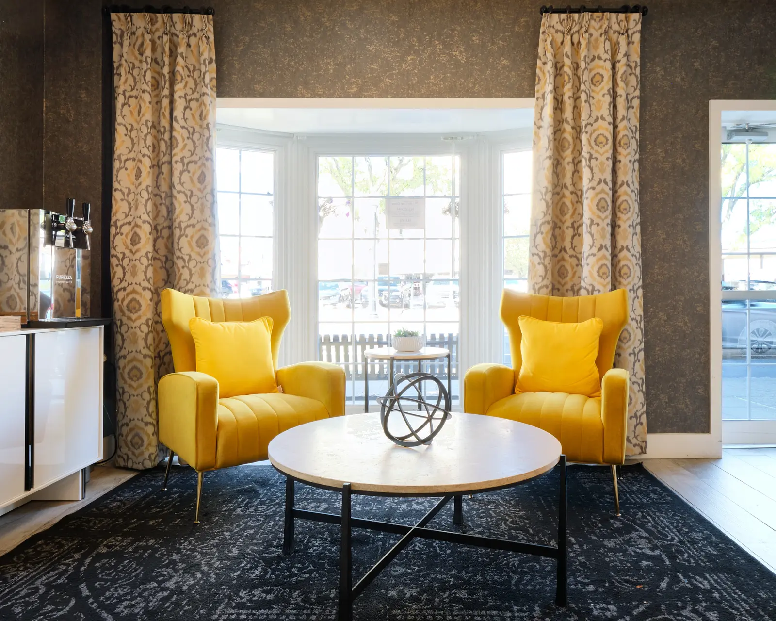 Two yellow chairs and a coffee table in a room with a beverage dispenser.