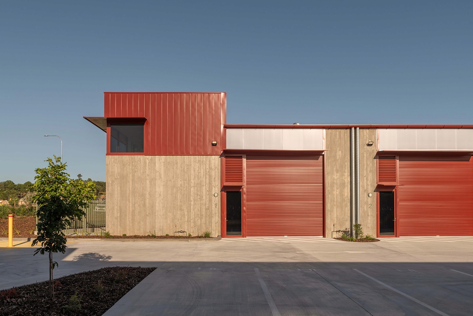 Front elevation of the RedSheds development, showing concrete industrial units with red metal cladding, large roller doors, and a clear, functional layout under open sky.