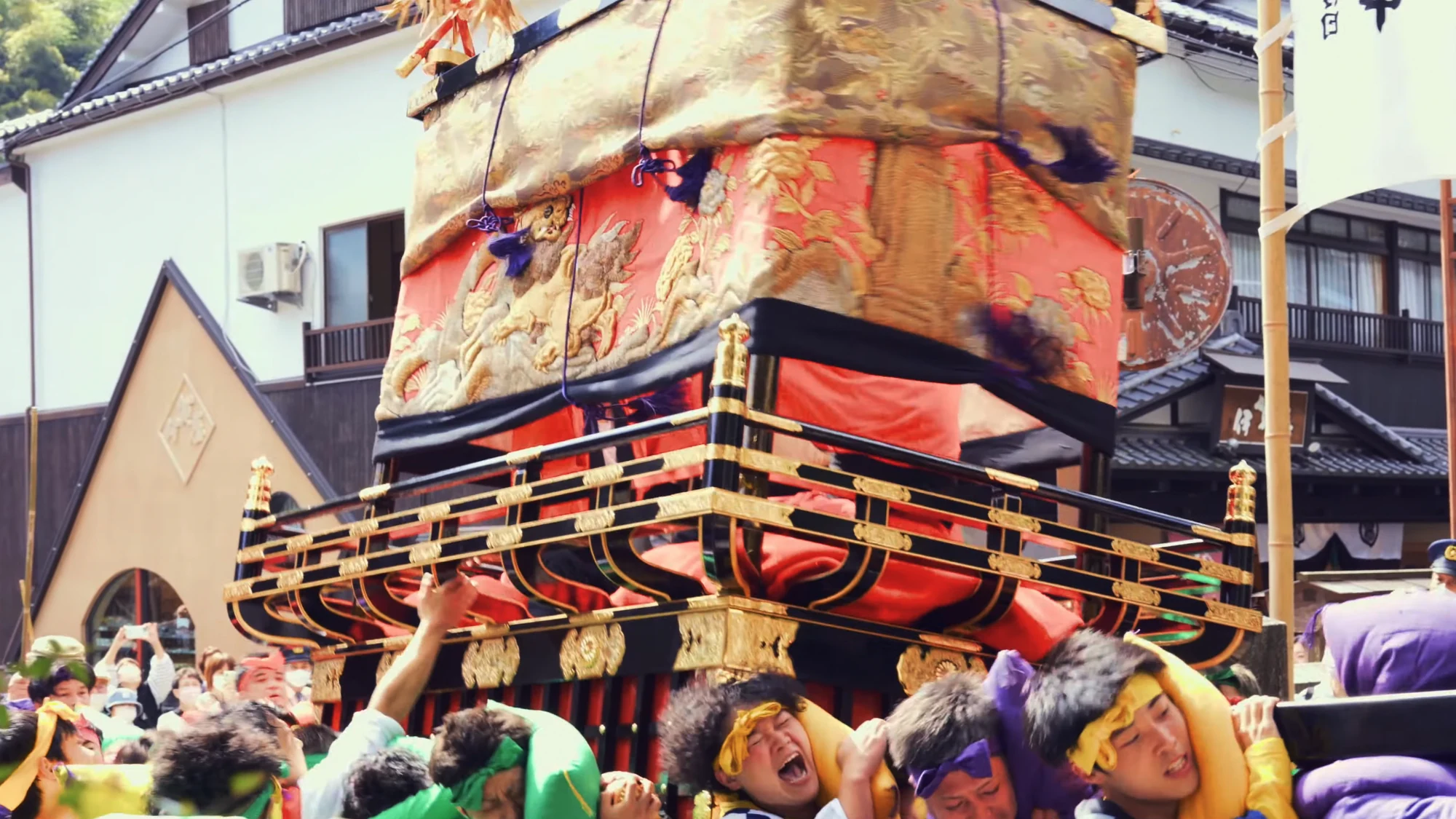 Bearers in happi coats crowded beneath a gilded festival float in a Kinosaki street.