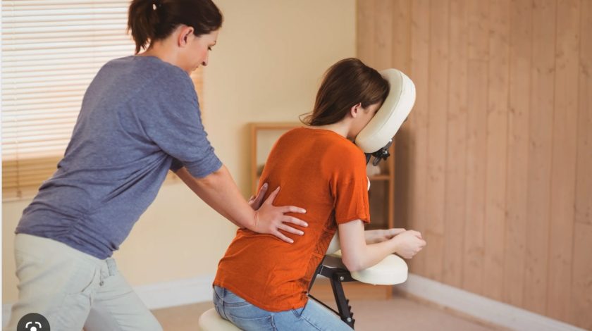A person receiving a seated massage in a cozy room, with wooden paneling and a window in the background, highlighting relaxation and wellness.