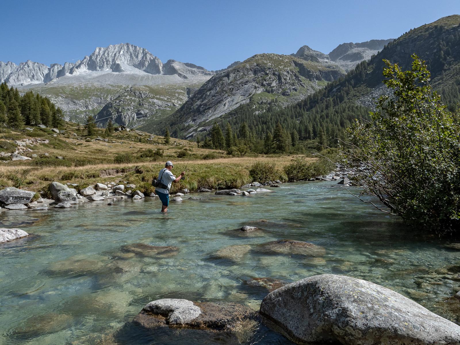 Hiker with a fishing rod enjoying a serene moment while fishing in the heart of the Italian Dolomites