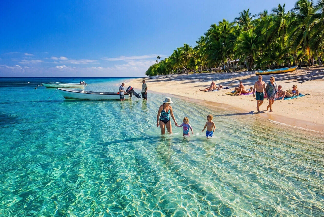 Several families with children gathered around the sandy beaches of Fiji walking slowly through the water