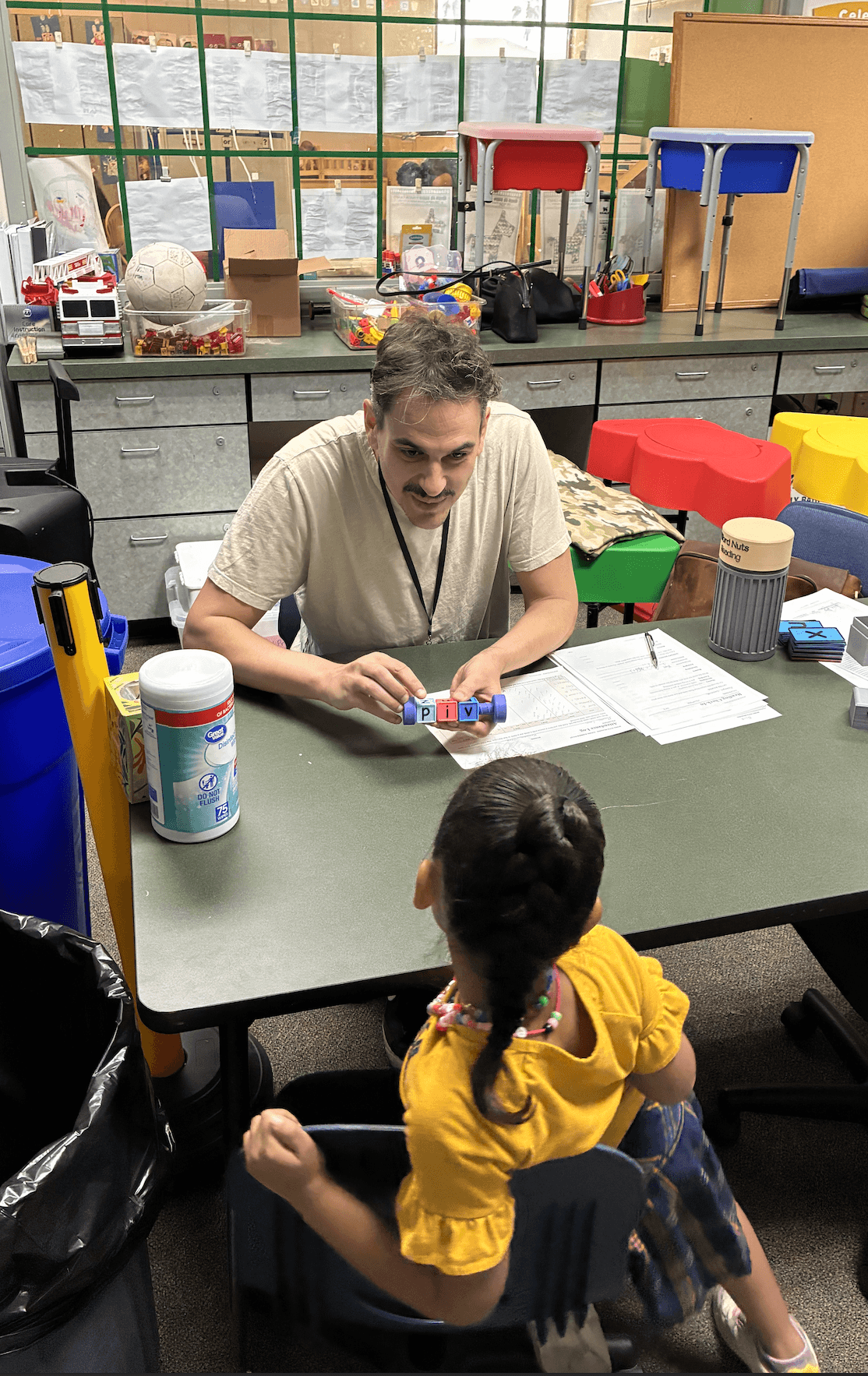 Michael Land, founder of Word Nuts Reading, holds the phonics bolt spelling P-I-V across a classroom table from a young student during a one-on-one blending session at a Coachella Valley Unified elementary school summer pilot phonics, phonemic awareness, reading intervention