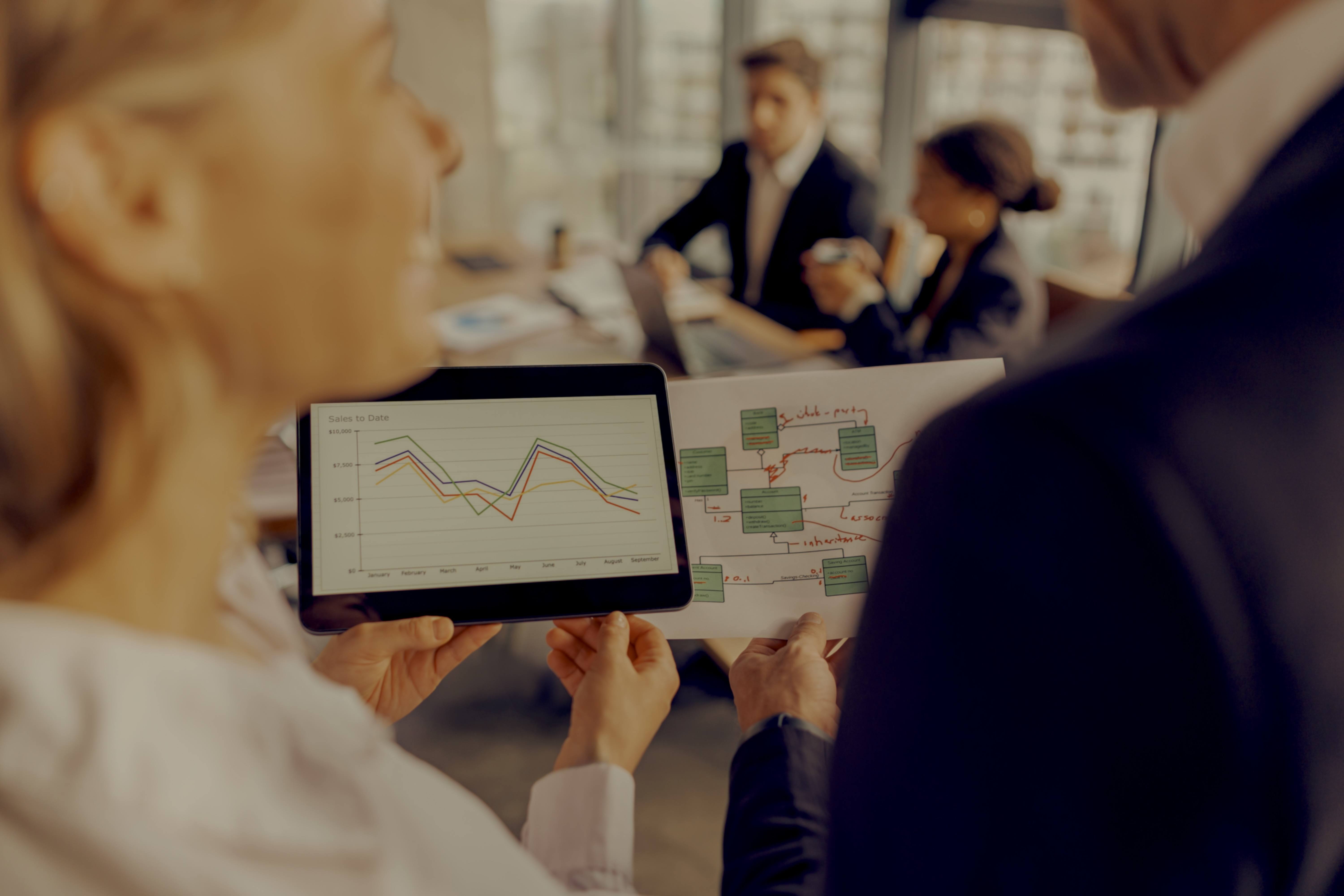 Colleagues looking at data and flowcharts on a tablet and A4 sheet