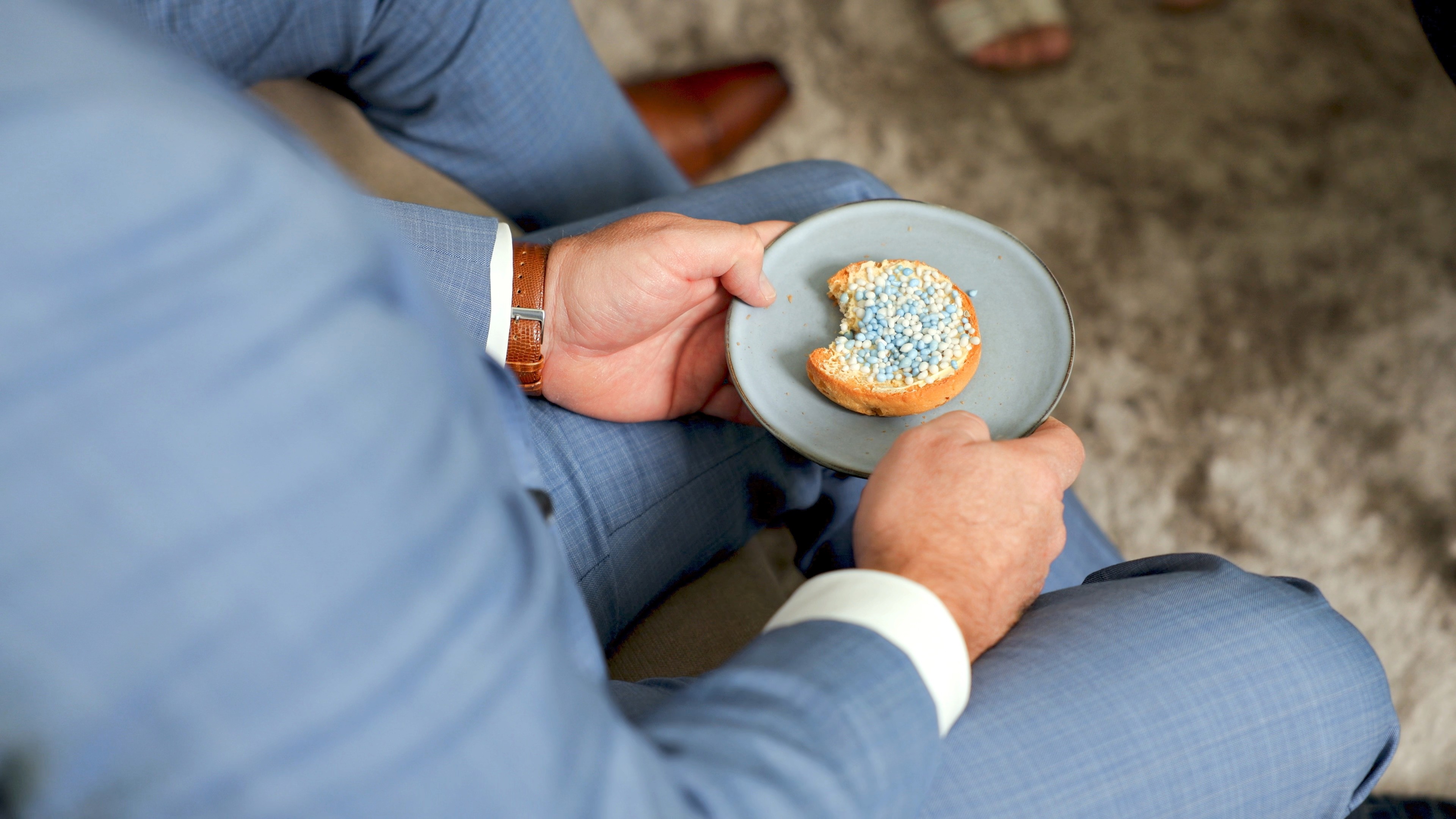  Bestuurder in pak met beschuit met muisjes in handen tijdens opname fusievideo Cedrah en RST zorgverleners