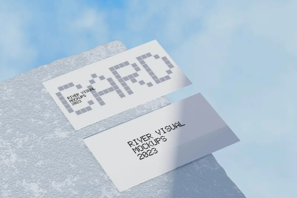 Two business cards with a minimalist grid-based design, placed on a textured stone surface. The cards are displayed in a bright, outdoor setting with a clear blue sky in the background.