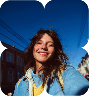 a brown woman with short hair wearing a blue jacket smiling while taking selfie with blue sky