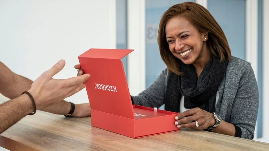 Women smiling down at a red box she has opened. Box reads 'KICKBOX' on the front of it.
