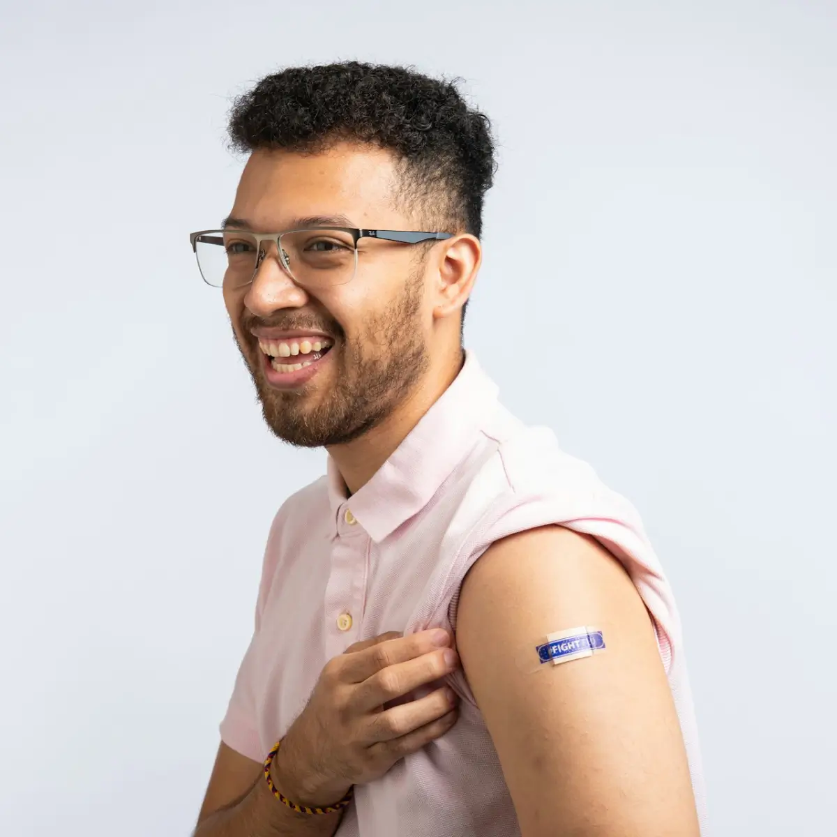 Smiling man wearing glasses and a pink shirt, showing his arm with a bandage after vaccination.