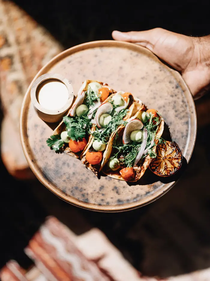 Three fish tacos served at Macondo restaurant in Nômade Tulum, Mexico, with a lime and sauce on the side, presented on a Mediterranean-style plate.