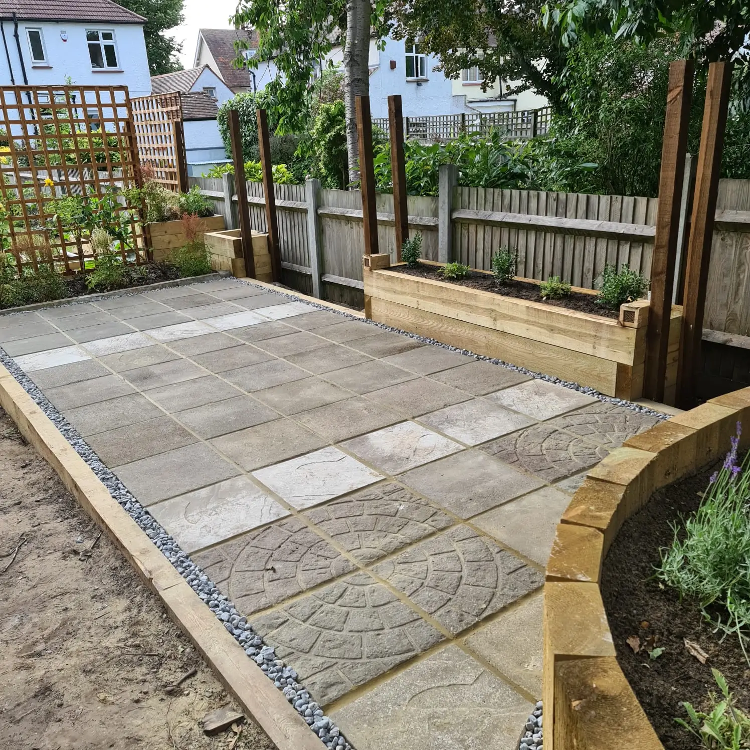 A newly paved garden area featuring rectangular stones, surrounded by wooden fences and greenery.