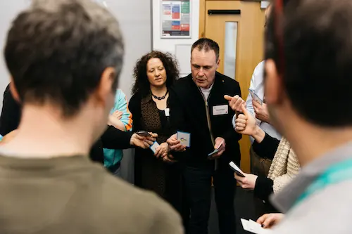 People talking and standing in a room, one holding an object.