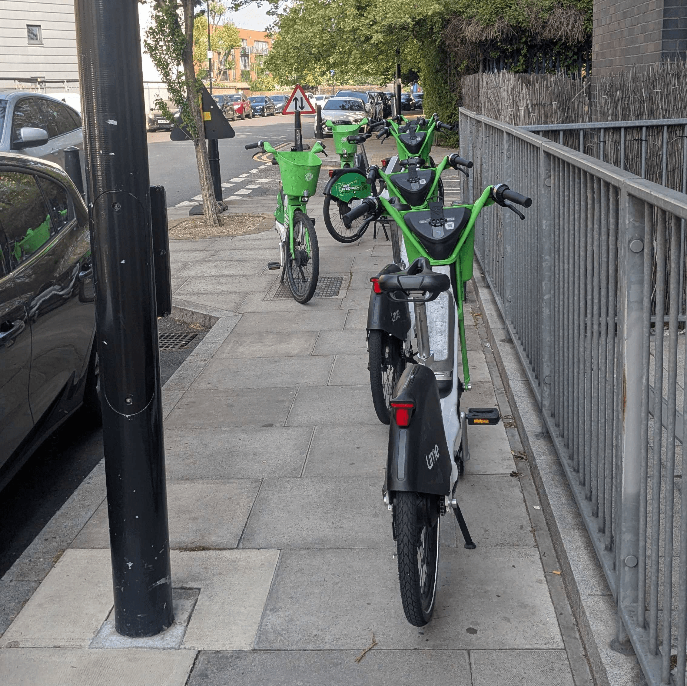 Seven e-bikes on a pavement next to a lampost obstructing the path through.