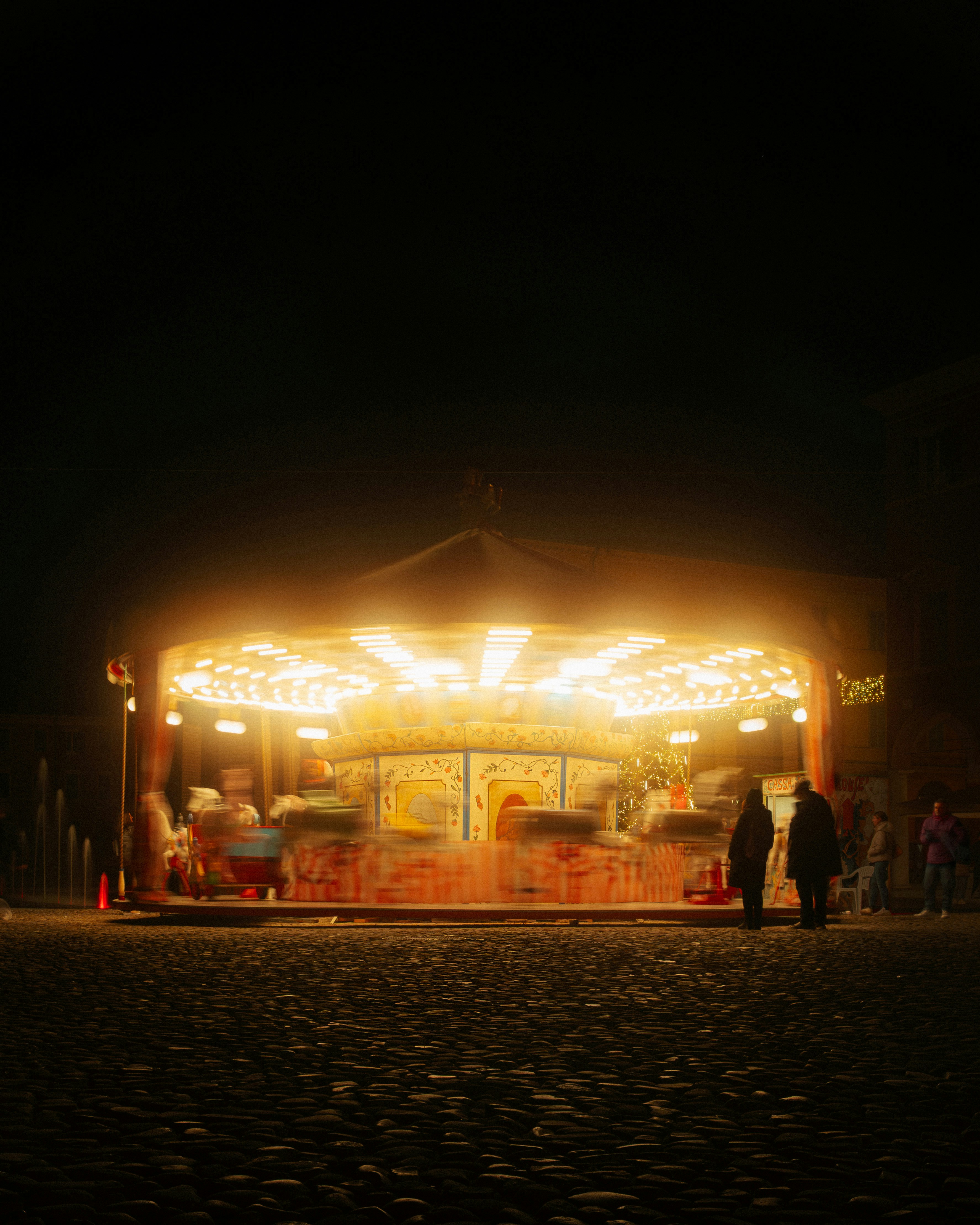 A brightly lit carousel at night with people watching.