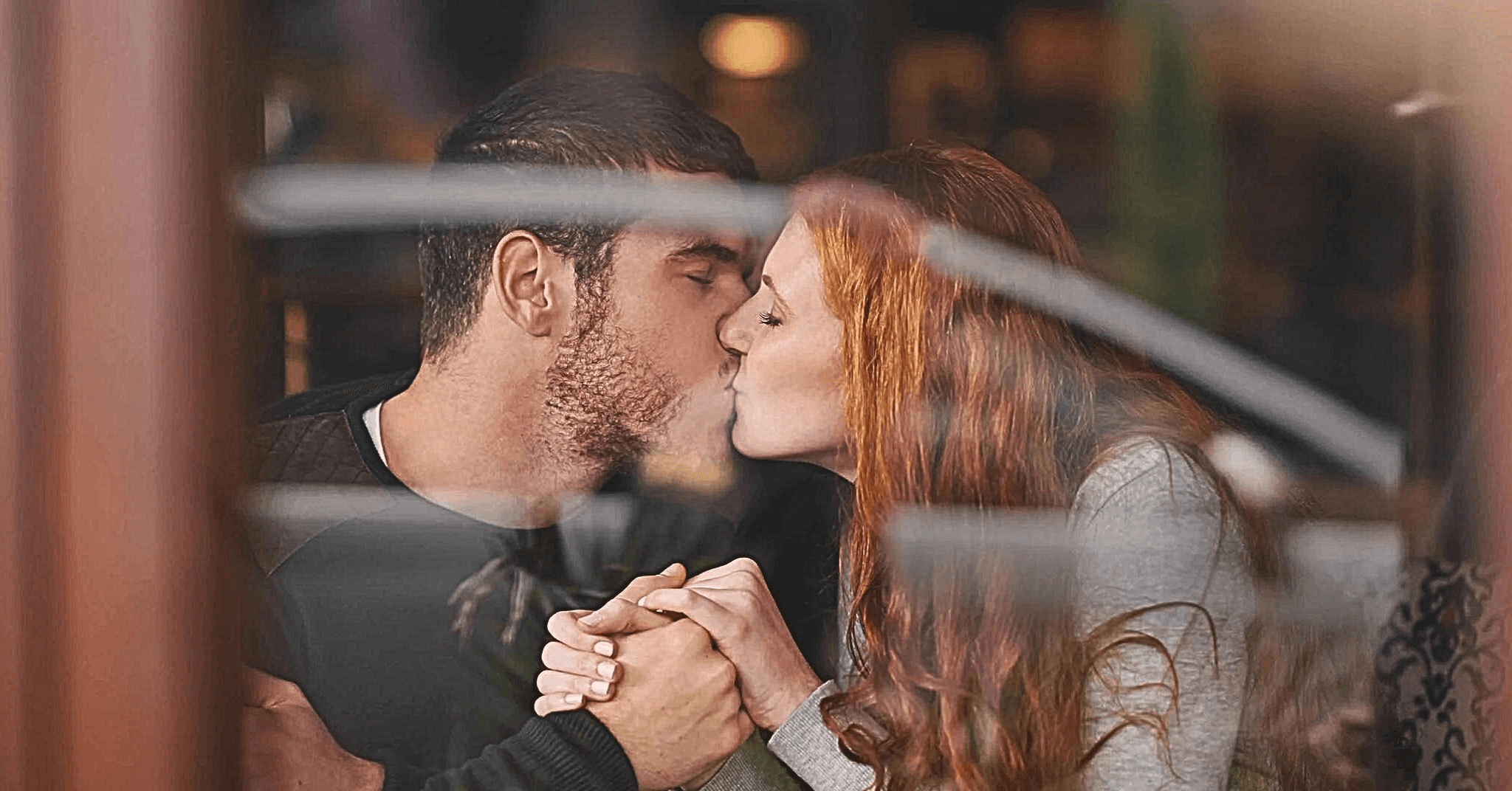 Par kysser og holder hender på et offentlig sted.