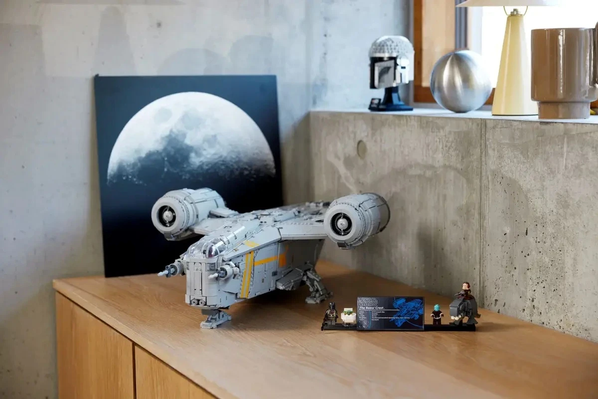 A detailed LEGO model spaceship sits on a wooden cabinet beside a poster of the moon and small figurines, creating a sci-fi themed display.