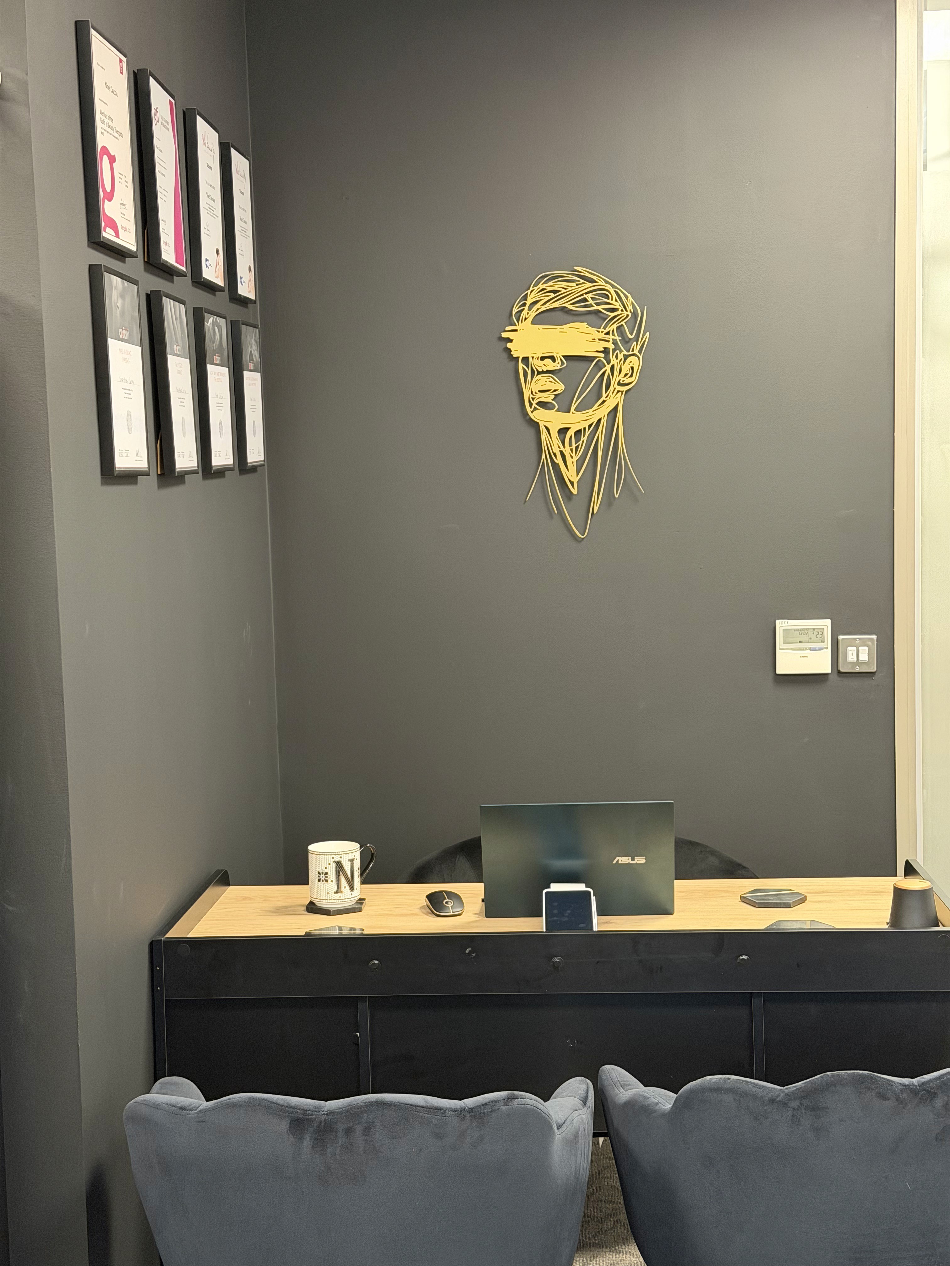 Office/Consultation section in the Manscaping salon, featuring velvet chairs, black rectangular desk with cream top, gold frame on the facing wall and, certificates in the left wall