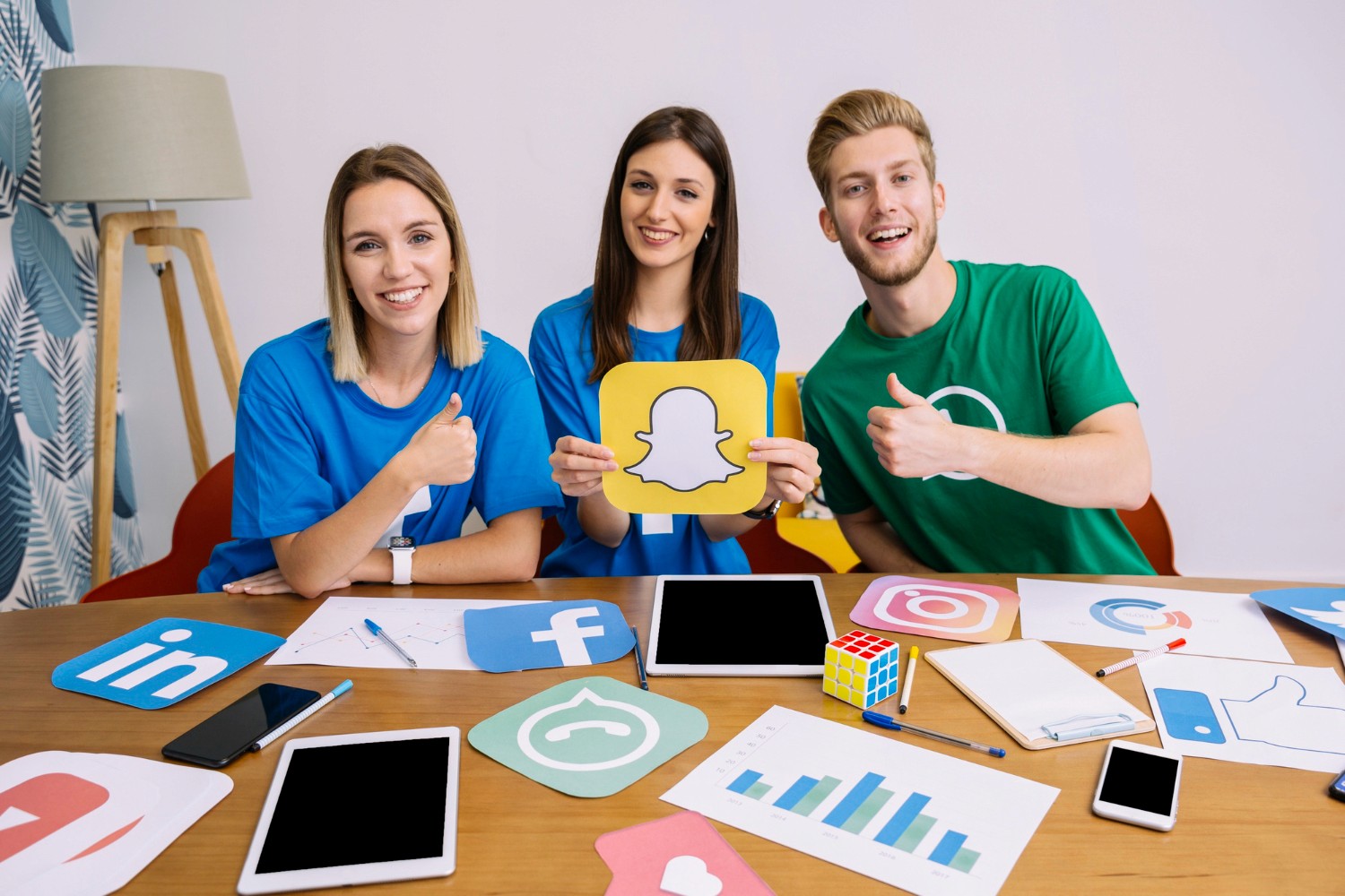  A table scene featuring three people discussing while social media icons are displayed around them.