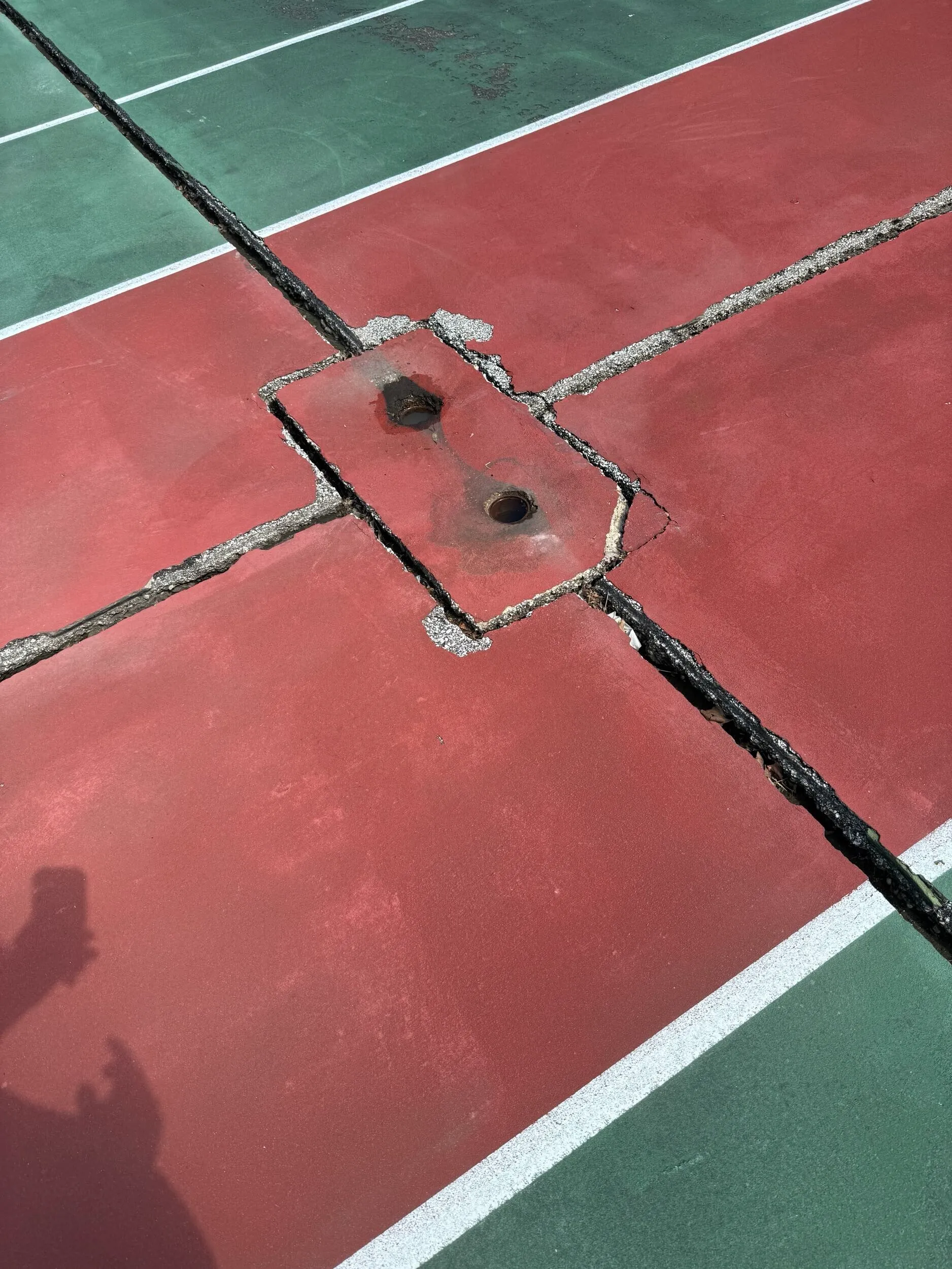 Severe cracking around an old tennis net post area before court conversion in Clinton Township, MI
