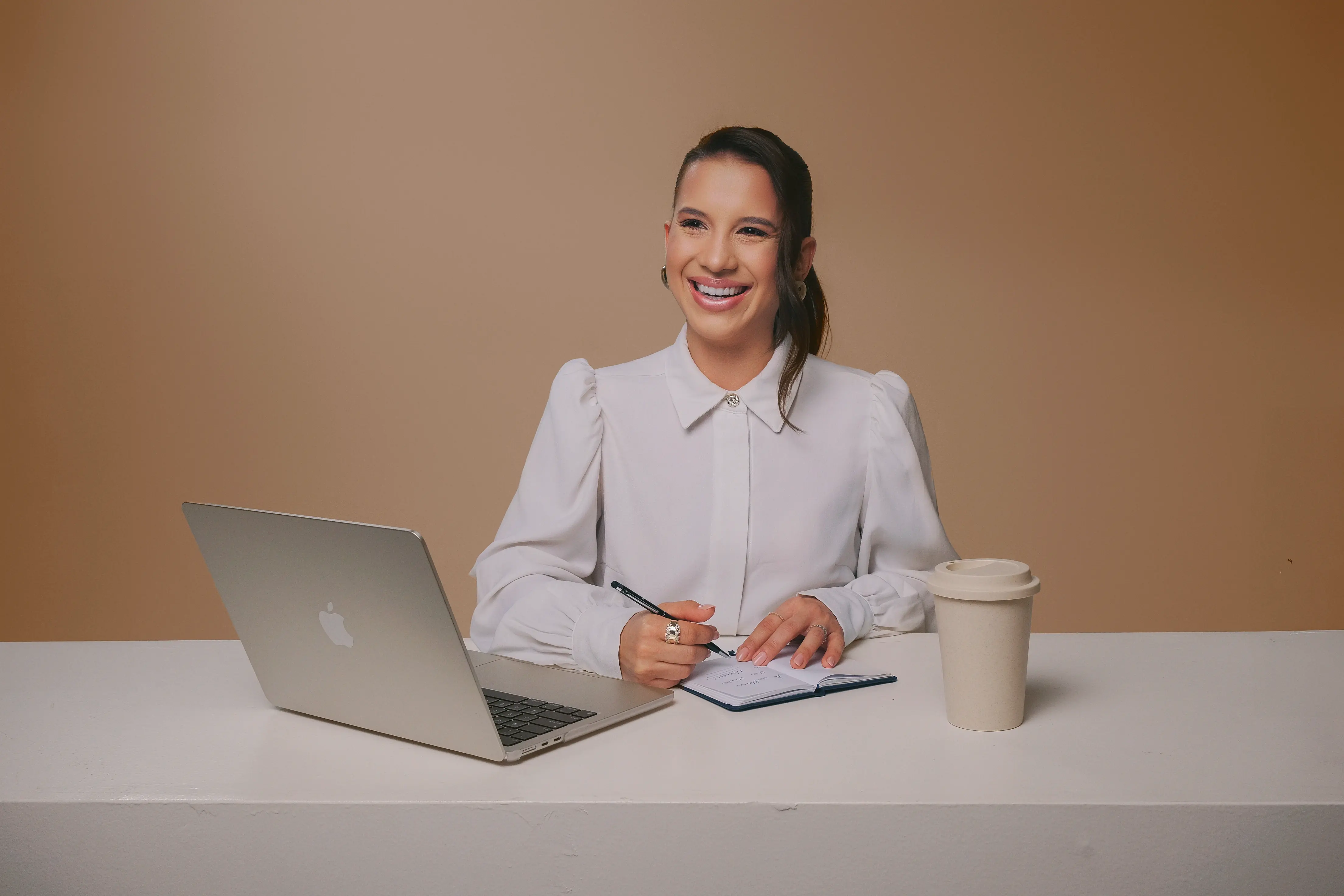 Isabela Ramos escrevendo em caderno com laptop e café na mesa – foto para site profissional