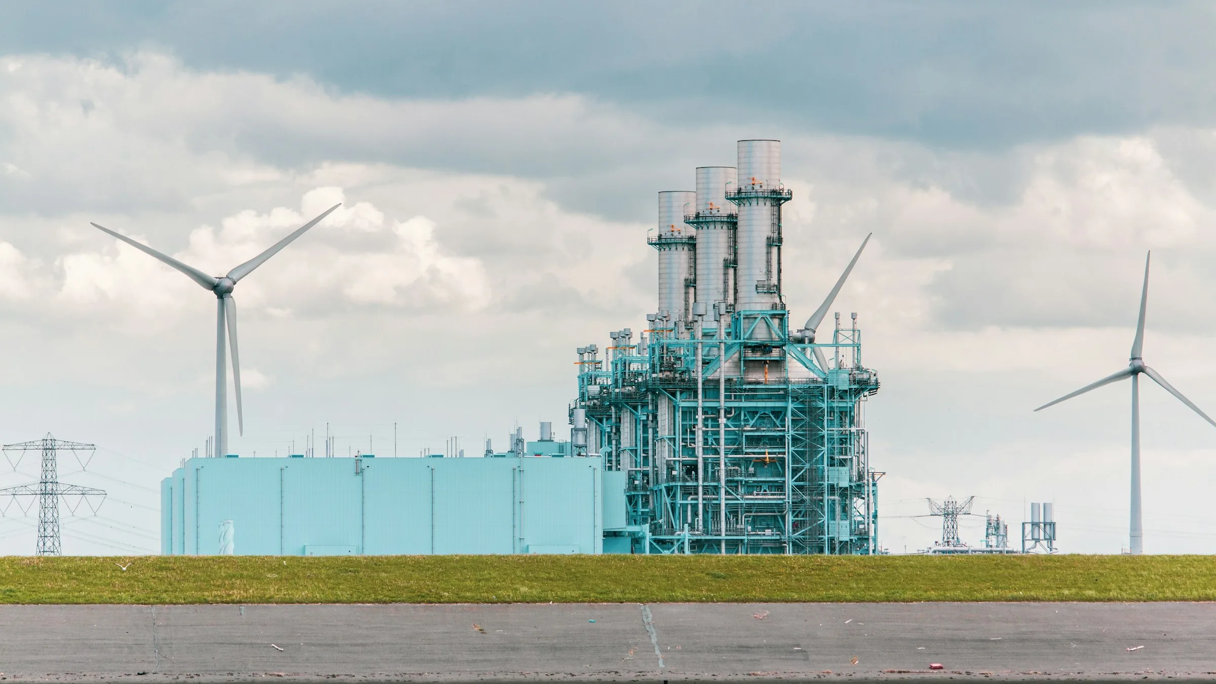 An industrial plant beside wind turbines on flat open land
