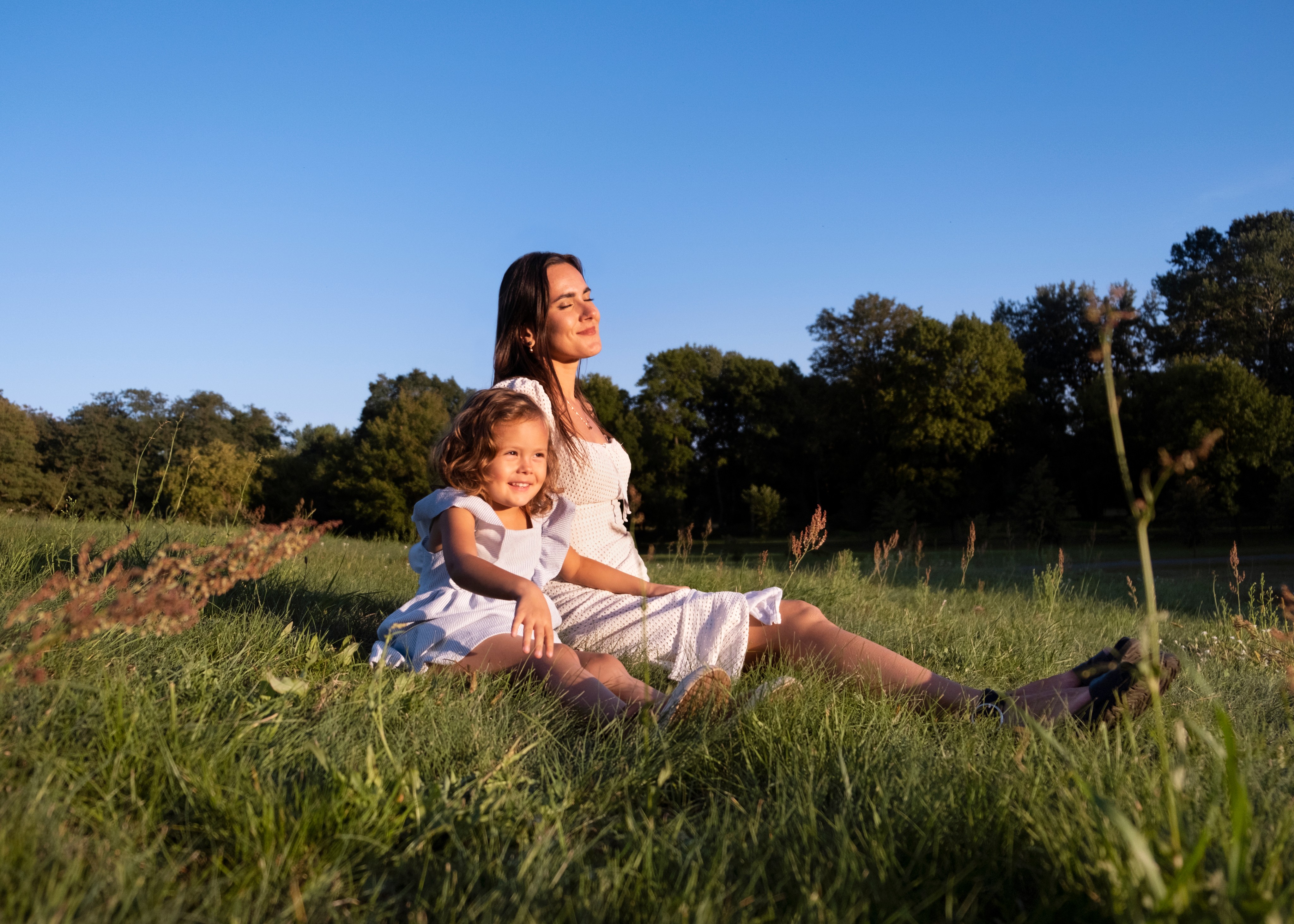 A mother and her daughter sitting in a sunny meadow