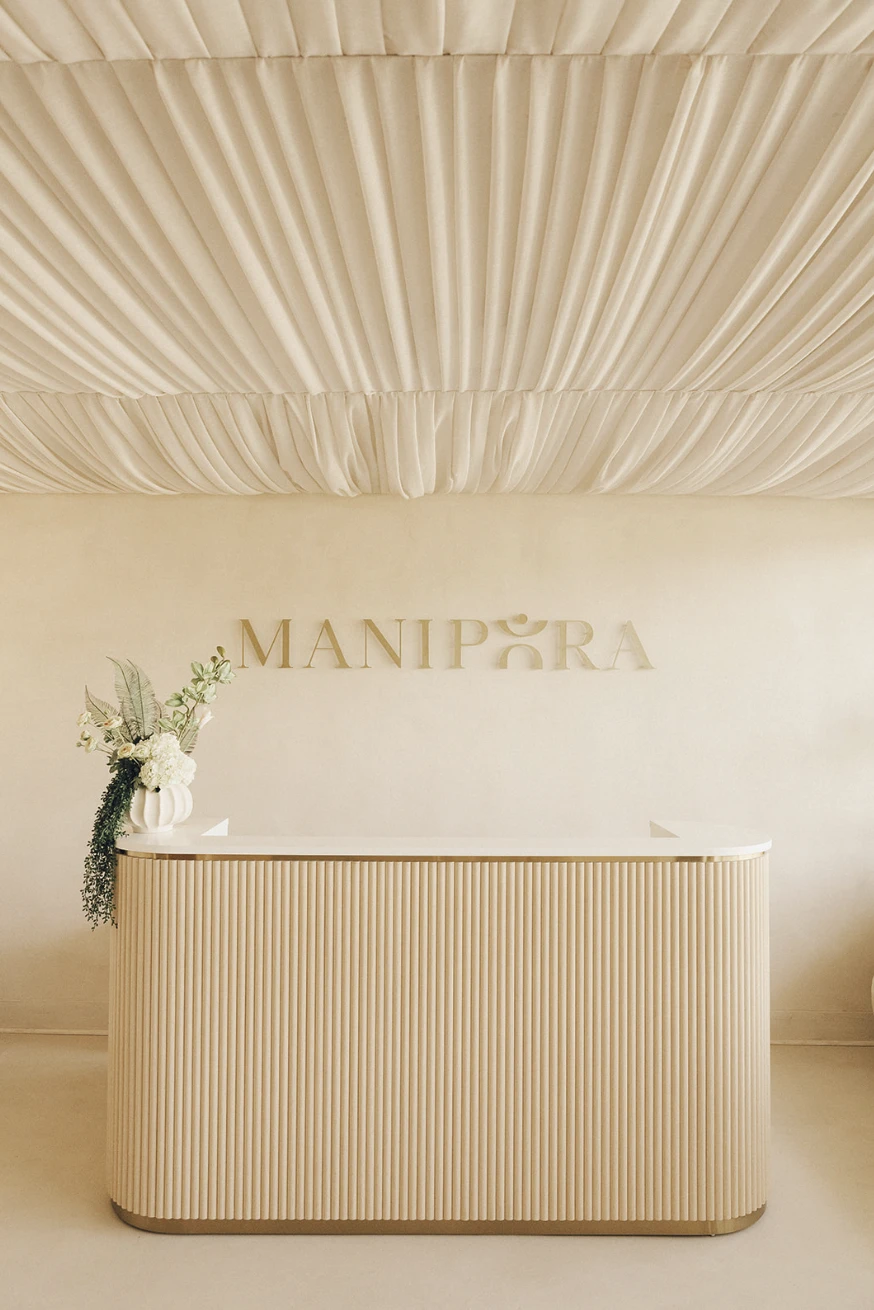 Manipura wellness studio reception with tonal wall signage above a curved fluted desk