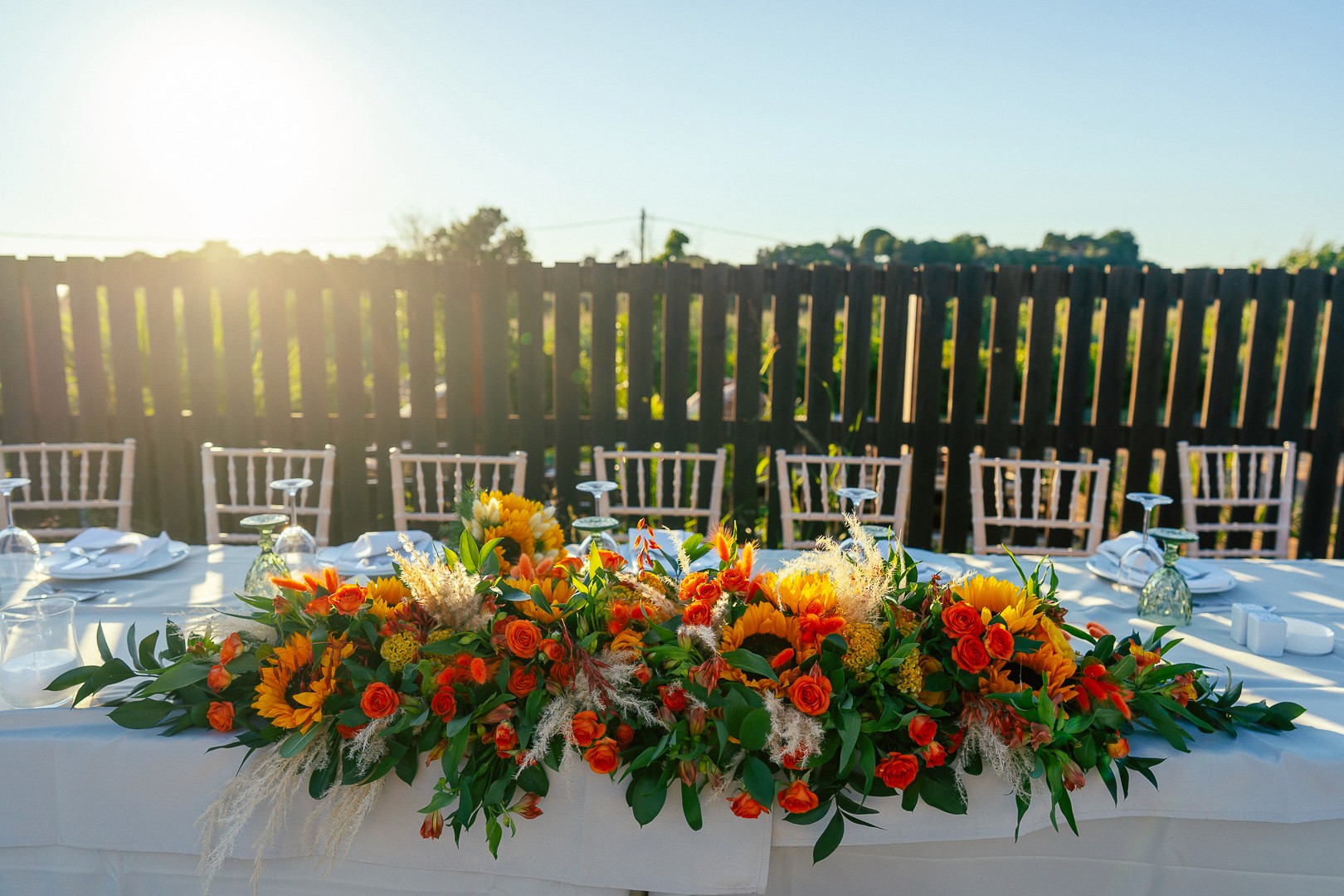 Εντυπωσιακός στολισμός τραπεζιού δεξίωσης γάμου με ηλιοτρόπια και πορτοκαλί τριαντάφυλλα στο ηλιοβασίλεμα