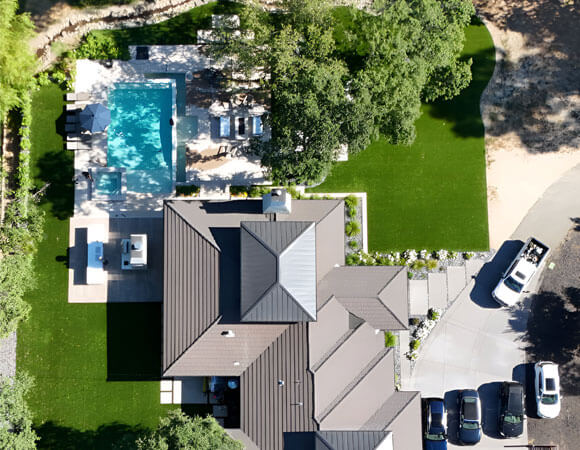 Drone shot high above a massive residence with large plots of green AGL Grass in both the front and backyards.