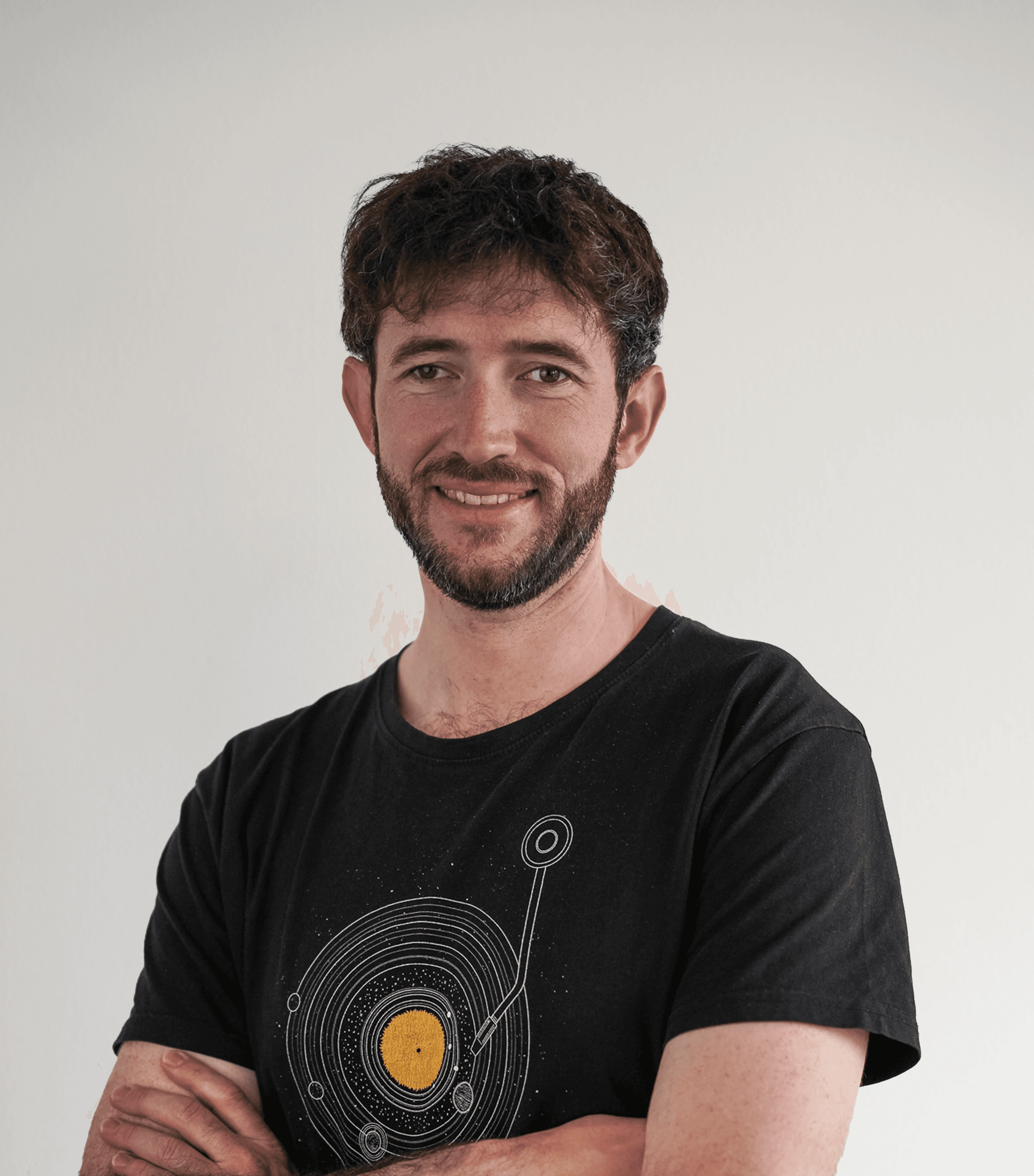 Man with dark brown hair and beard wearing a black t-shirt and smiling in front of purple background.
