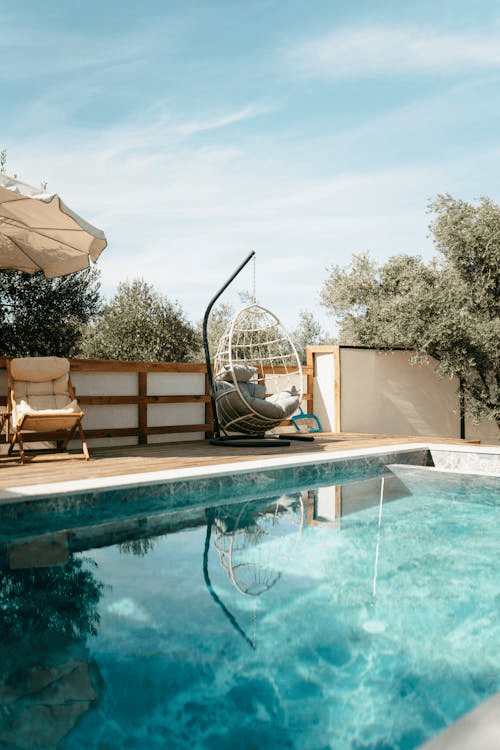 Luxury infinity pool overlooking the ocean from a terrace with white railing under a clear blue sky.
