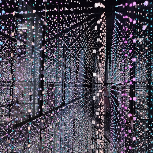 A reflective room filled with hanging multicolored LED lights, creating an immersive, infinite light effect.