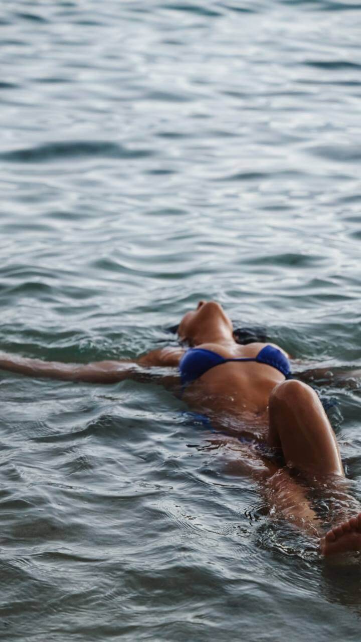 a person wearing a blue bikini floats with their arms wide and head back in the ocean