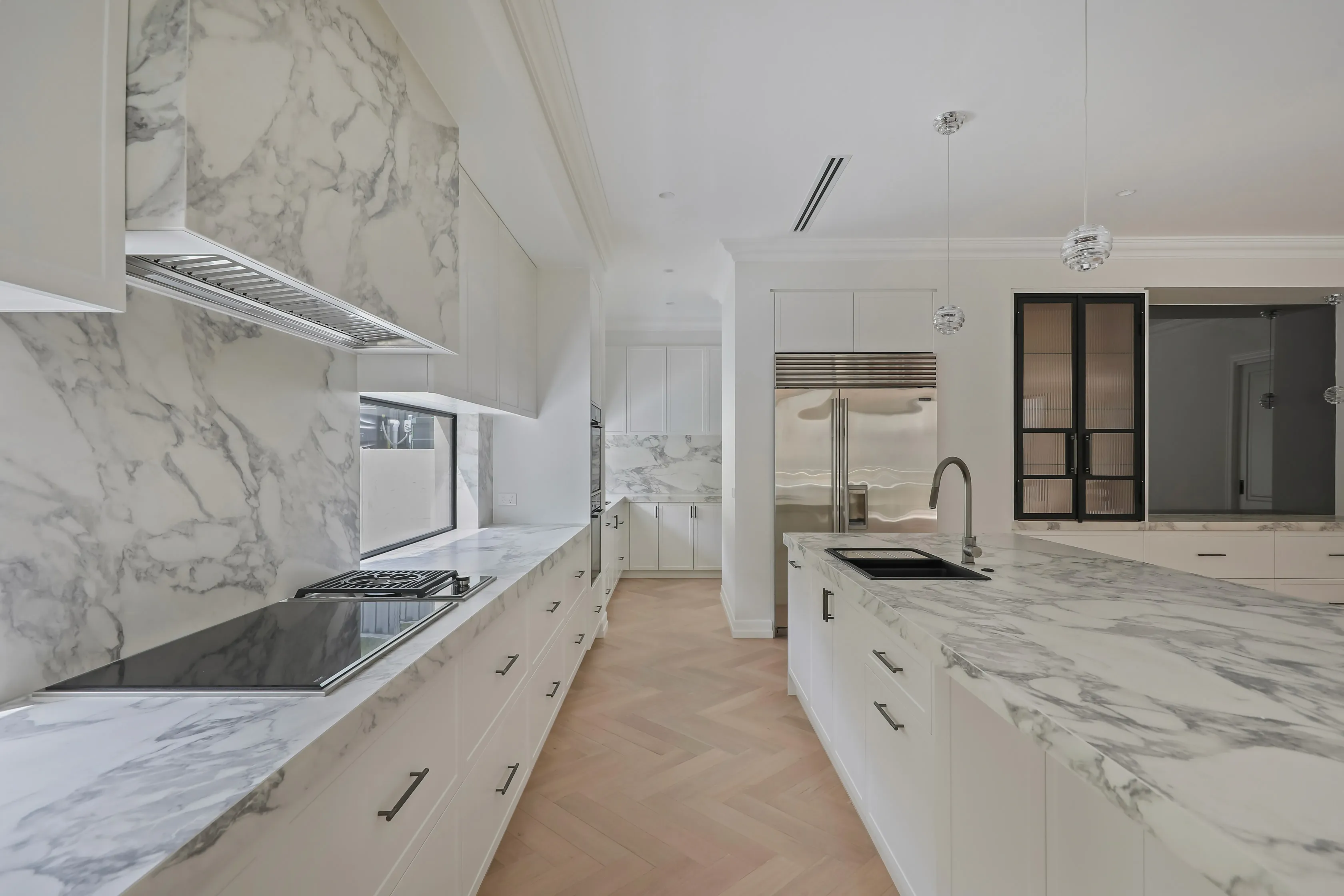 Templestowe galley kitchen with marble benchtops and splashback, integrated rangehood and a fluted-glass black-framed cabinet