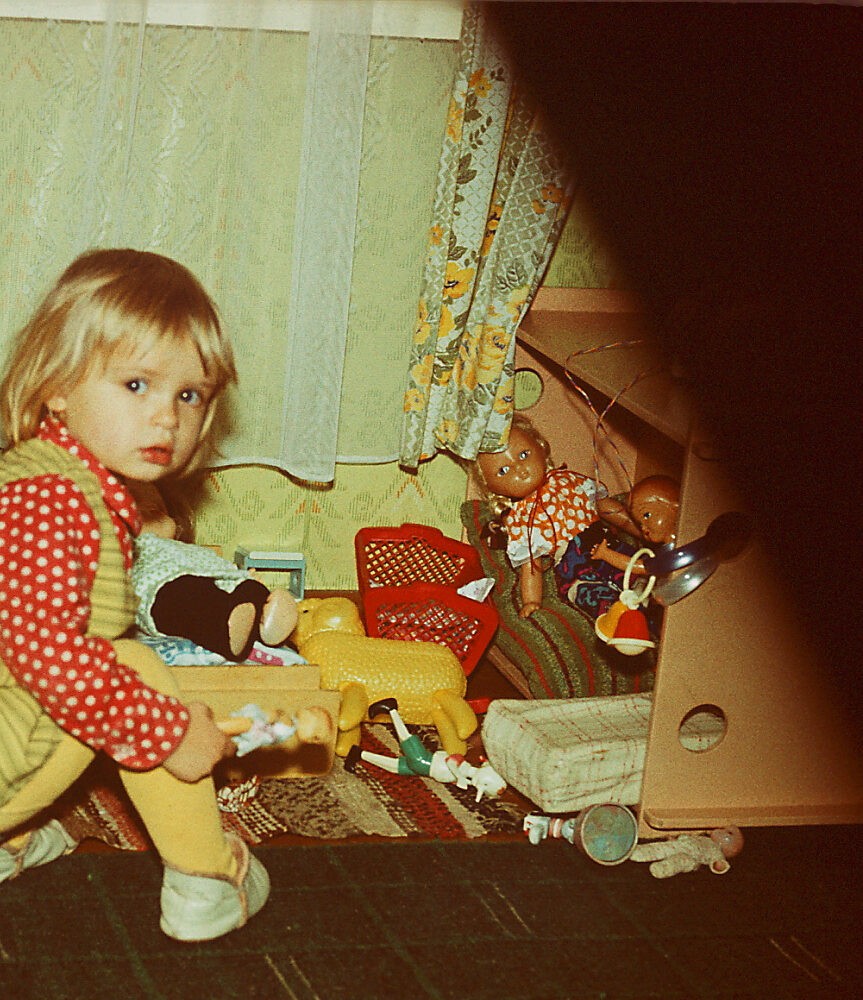 Väike tüdruk mängib mänguasjadega ja vaatab kaamera poole
