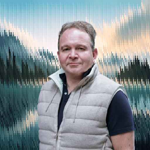 Professional portrait of a man in casual attire against a scenic outdoor background.