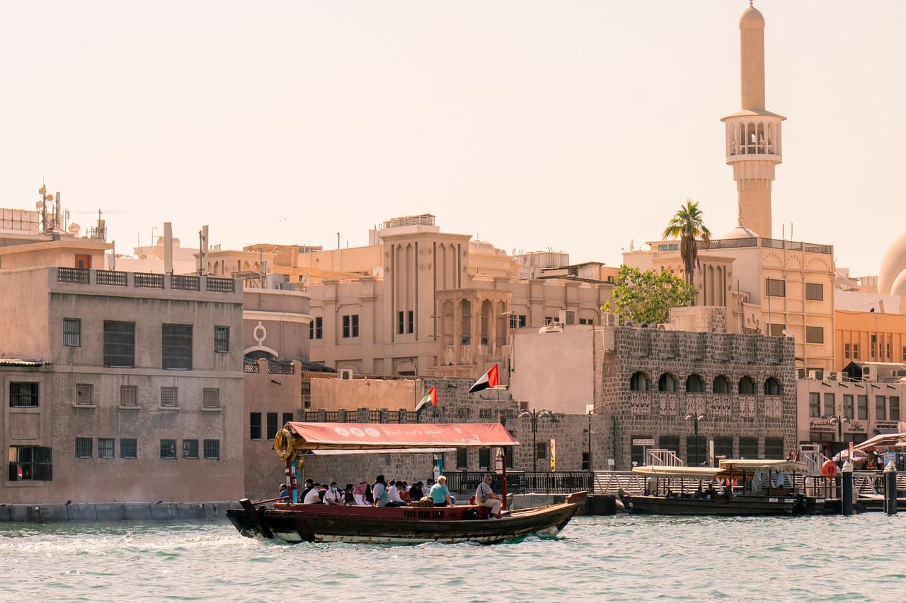 People riding an Abra boat on calm waters, with beige-colored buildings in the background, part of things to do in Dubai with family.