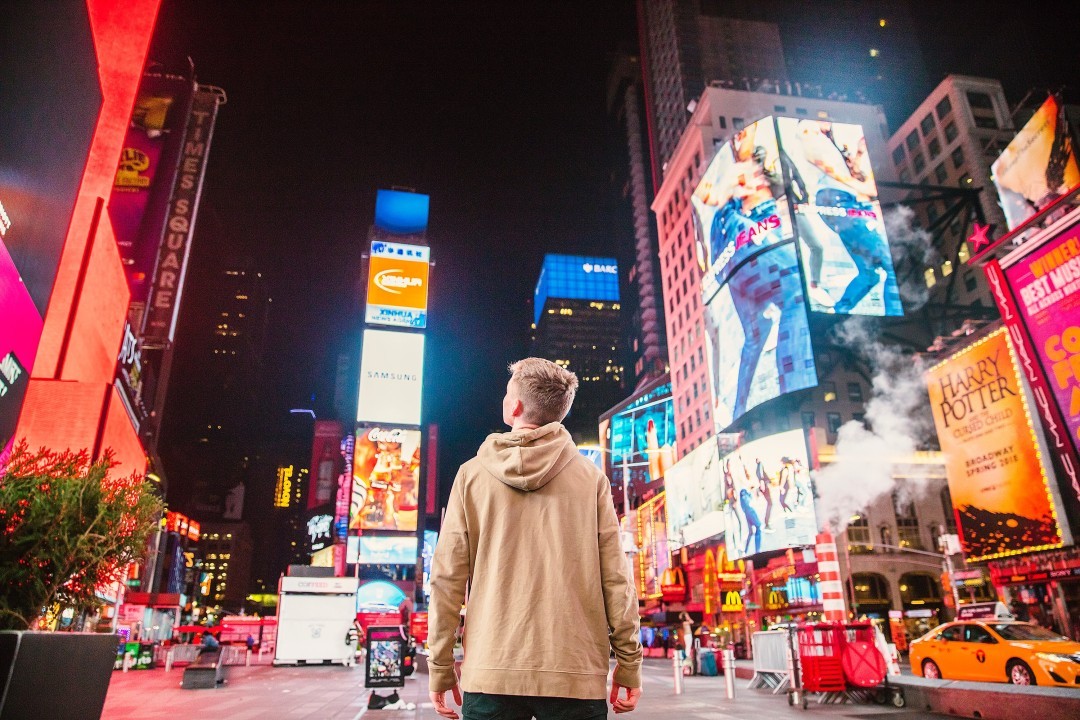 Person standing in Times Square surrounded by large digital billboards and illuminated outdoor advertisements at night.