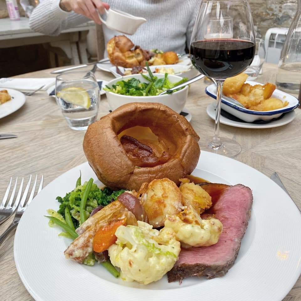 Traditional Sunday roast dinner with Yorkshire pudding, roast beef, potatoes and seasonal vegetables served with red wine